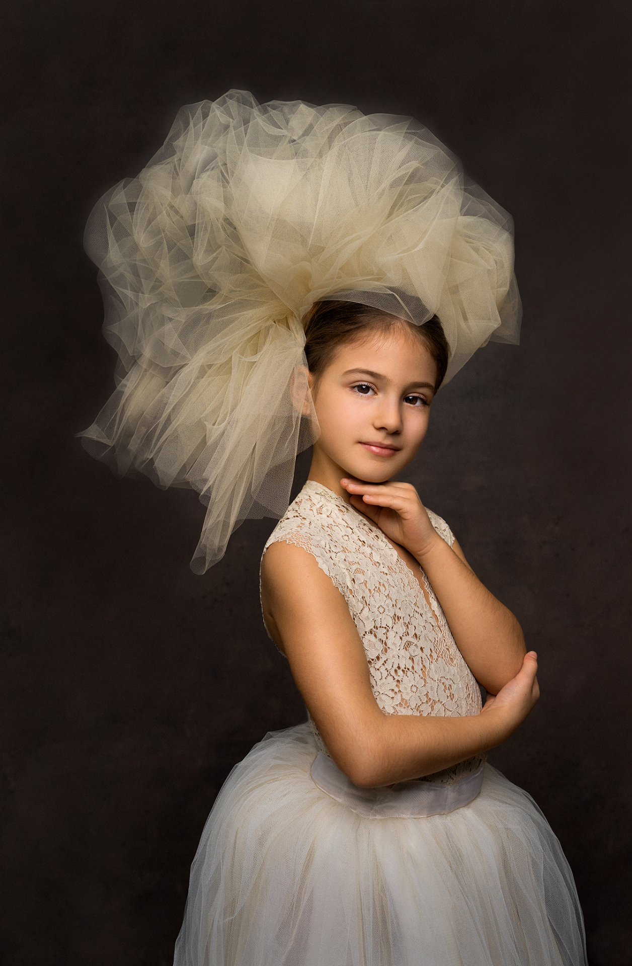 Ritratto elegante di bambina in abito da ballerina con copricapo in tulle beige, su sfondo scuro, scattato da Claudia Spaziani nel suo studio fotografico a Bologna.