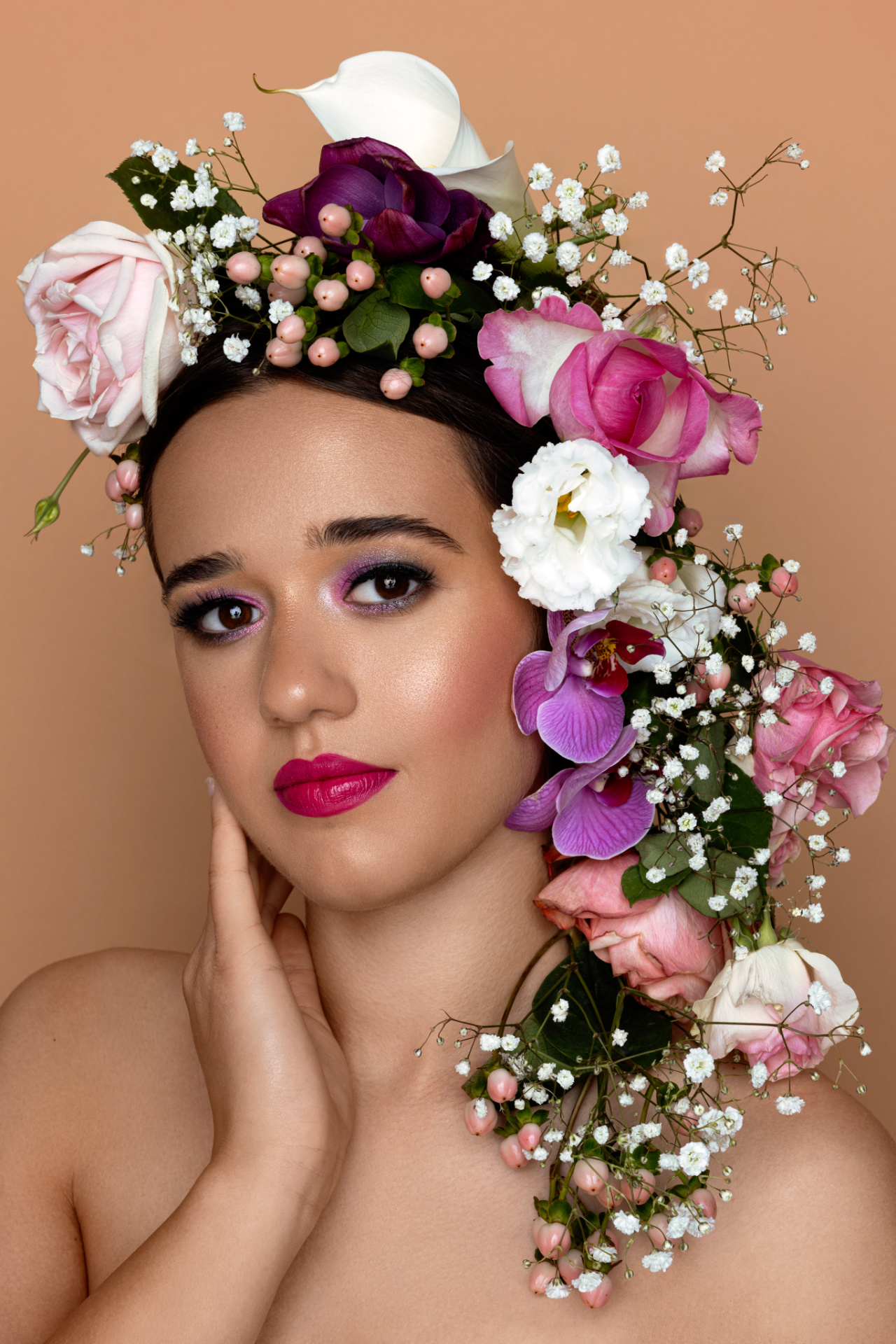 Ritratto creativo di adolescente con composizione floreale su capo e spalla, trucco vivace e sfondo pesca, scattato da Claudia Spaziani nel suo studio fotografico a Bologna.