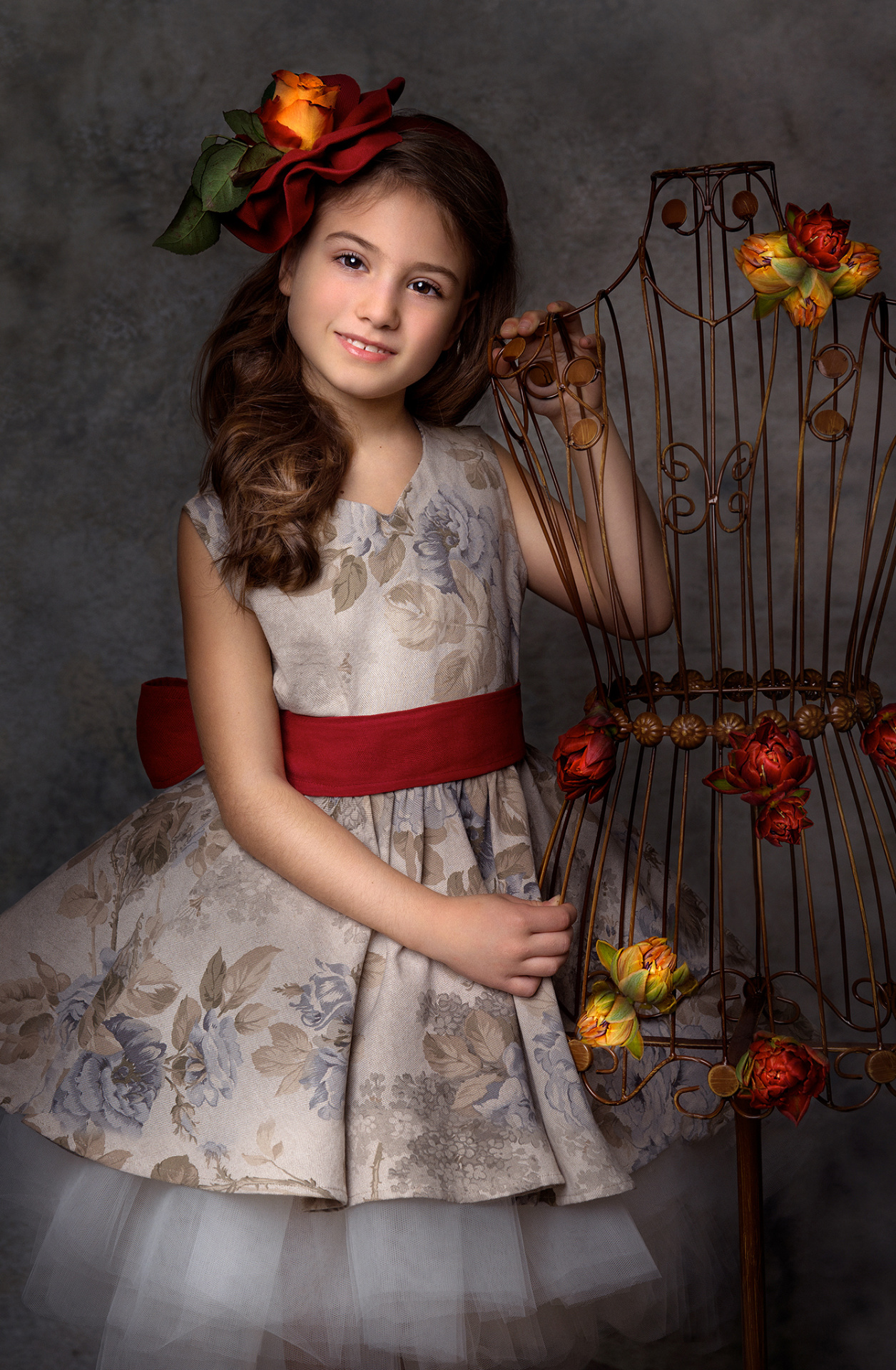 Ritratto classico di bambina in abito floreale con gonna in tulle e piume rosse, realizzato da Claudia Spaziani nel suo studio fotografico a Bologna.