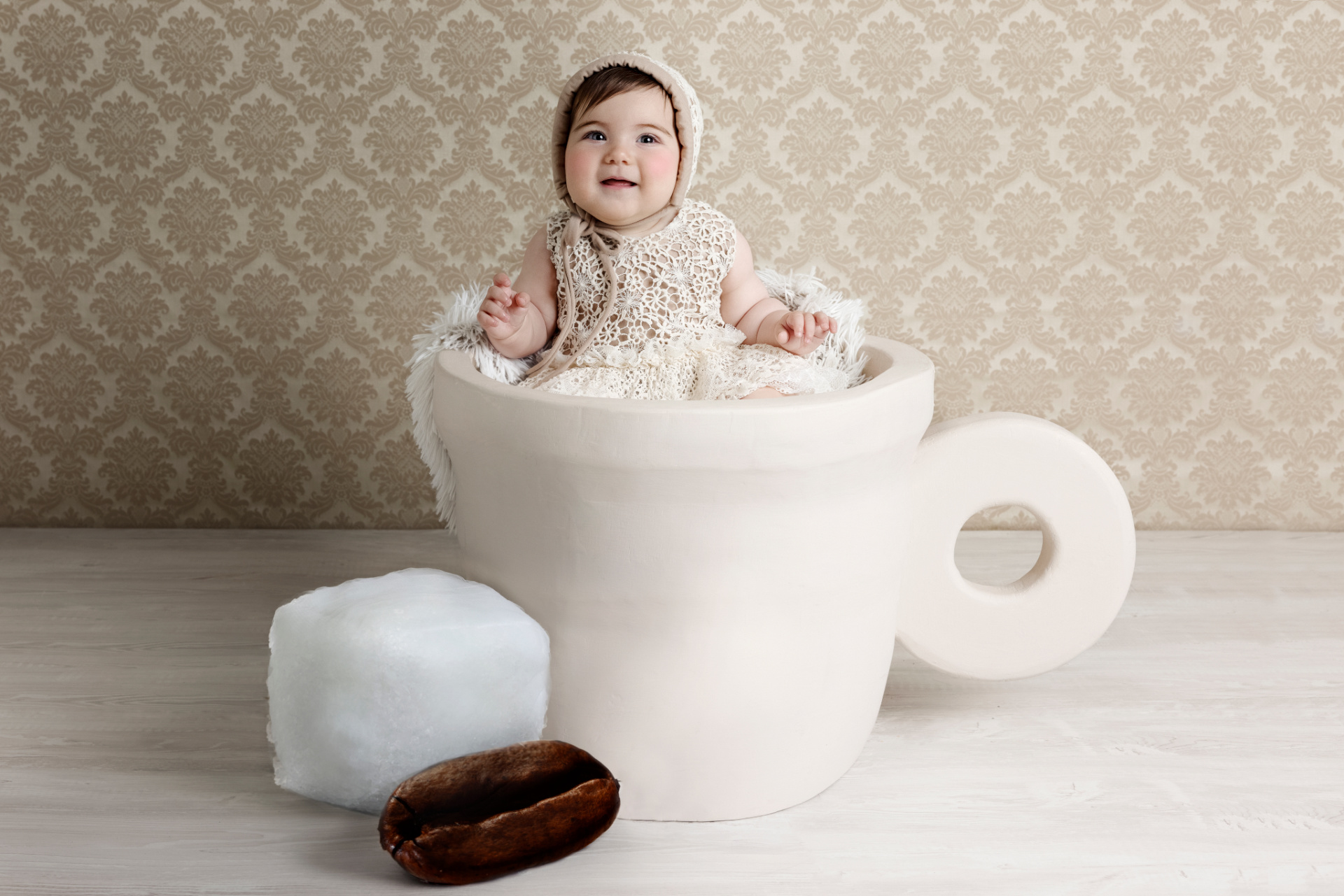 Foto originale di bambina di 6 mesi in tazza oversize con abito all’uncinetto e sfondo damascato, scattata da Claudia Spaziani nel suo studio fotografico a Bologna.