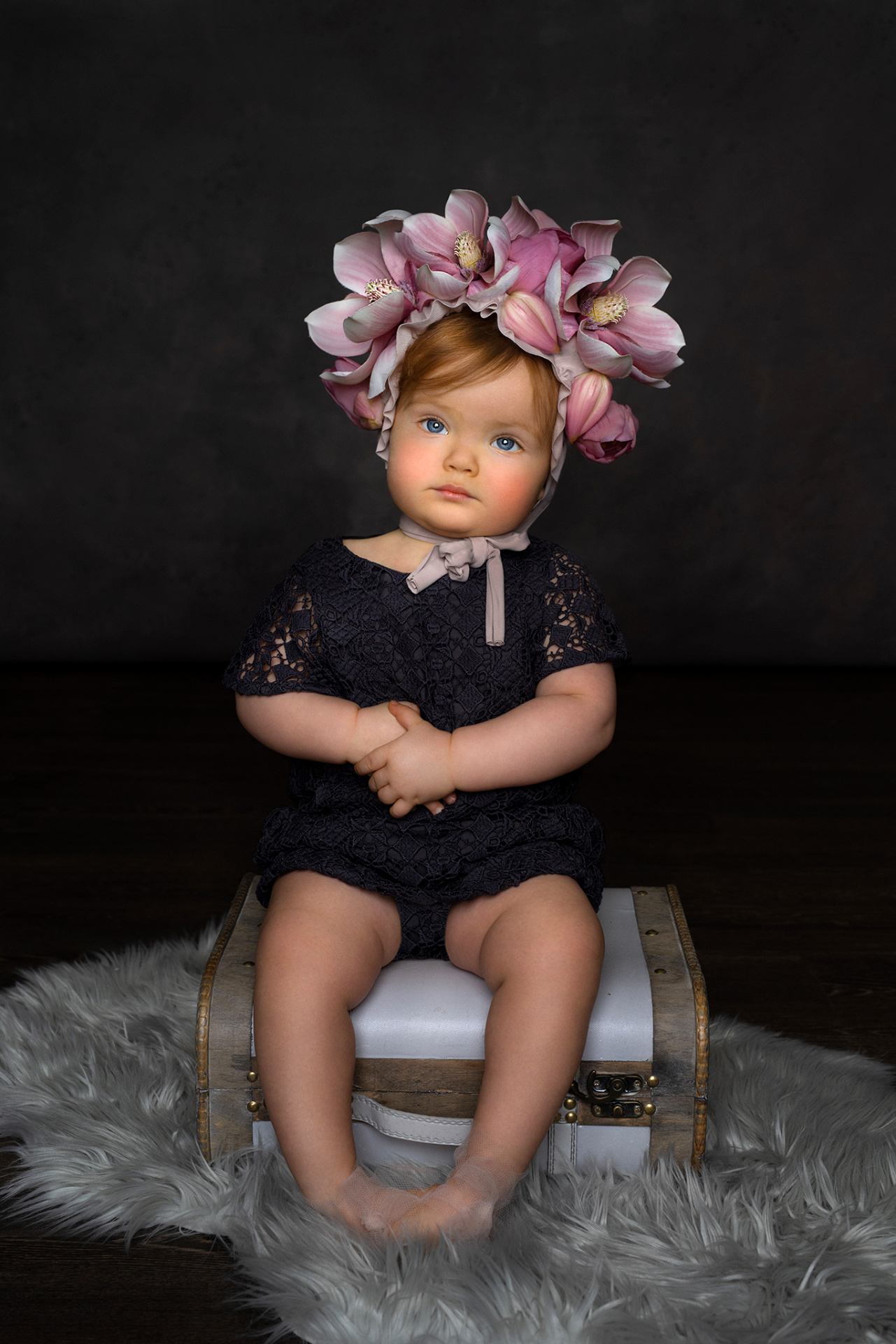 Ritratto in studio di bambina con copricapo floreale rosa e viola, seduta su una valigia vintage, realizzato dalla fotografa Claudia Spaziani a Bologna.