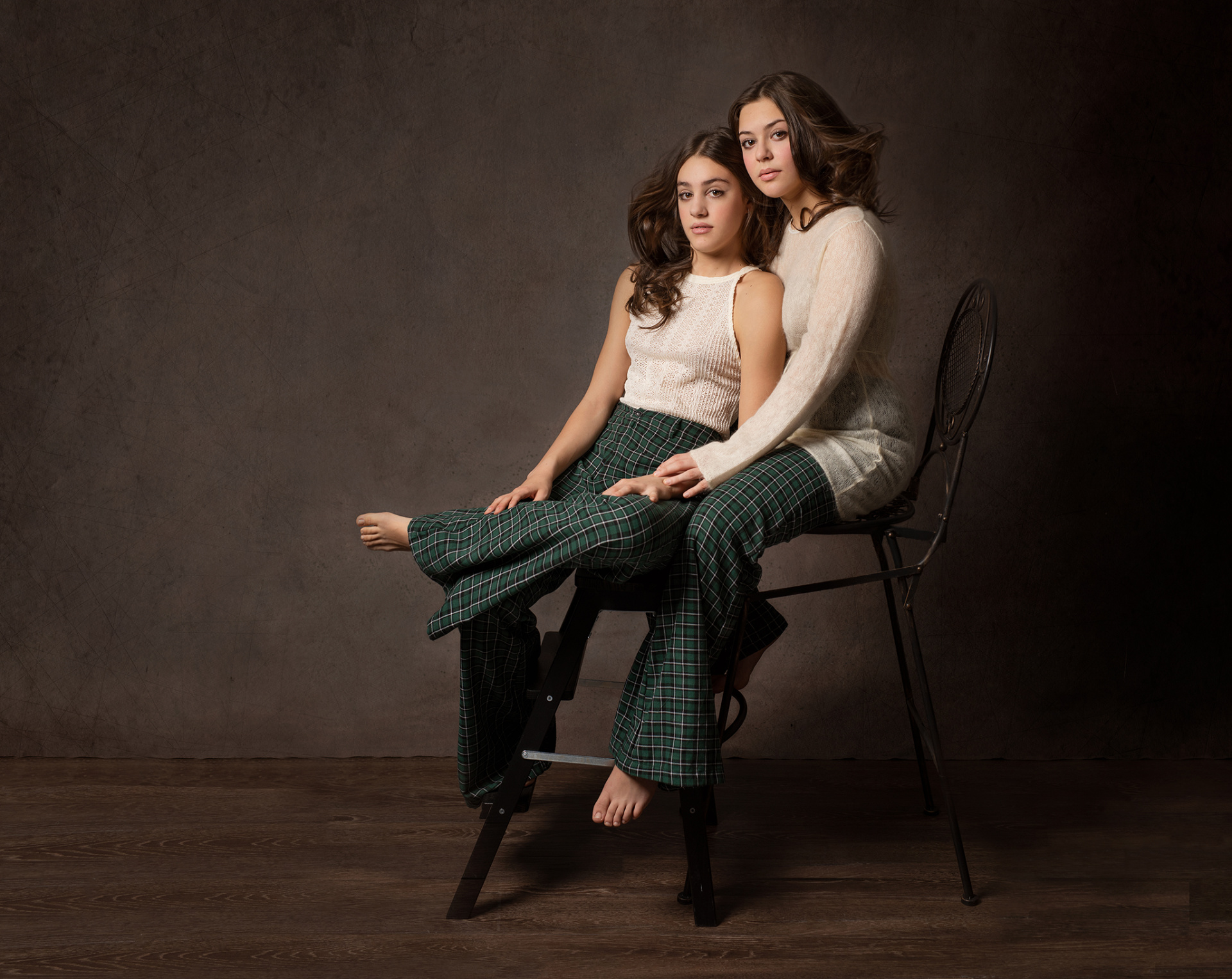 Due adolescenti in posa simmetrica con pantaloni scozzesi verdi e top crema, ritratti in studio da Claudia Spaziani a Bologna.