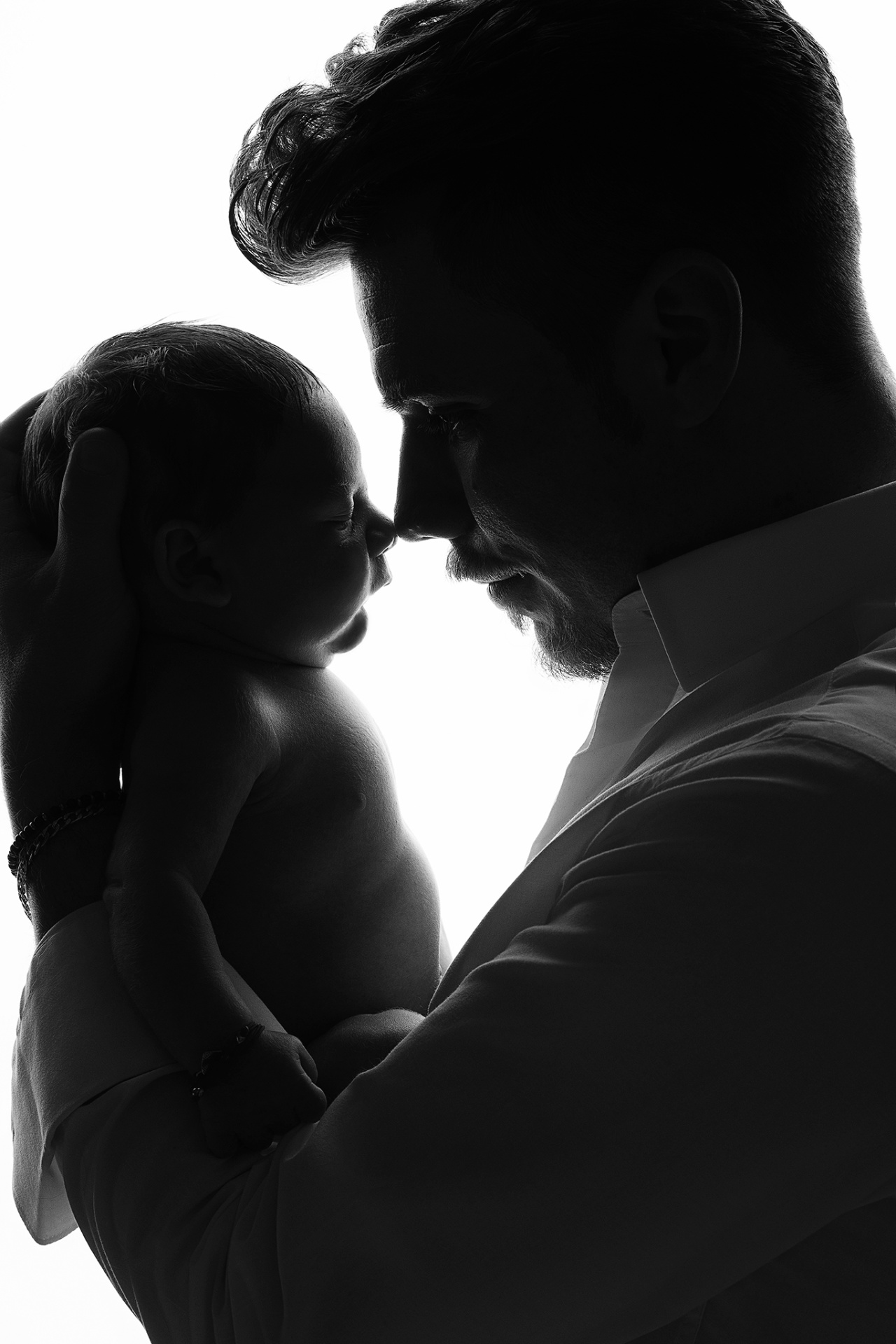 Fotografia artistica in bianco e nero in silhouette di padre che culla neonato maschio, realizzata da Claudia Spaziani fotografa a Bologna. Immagine intima e suggestiva.