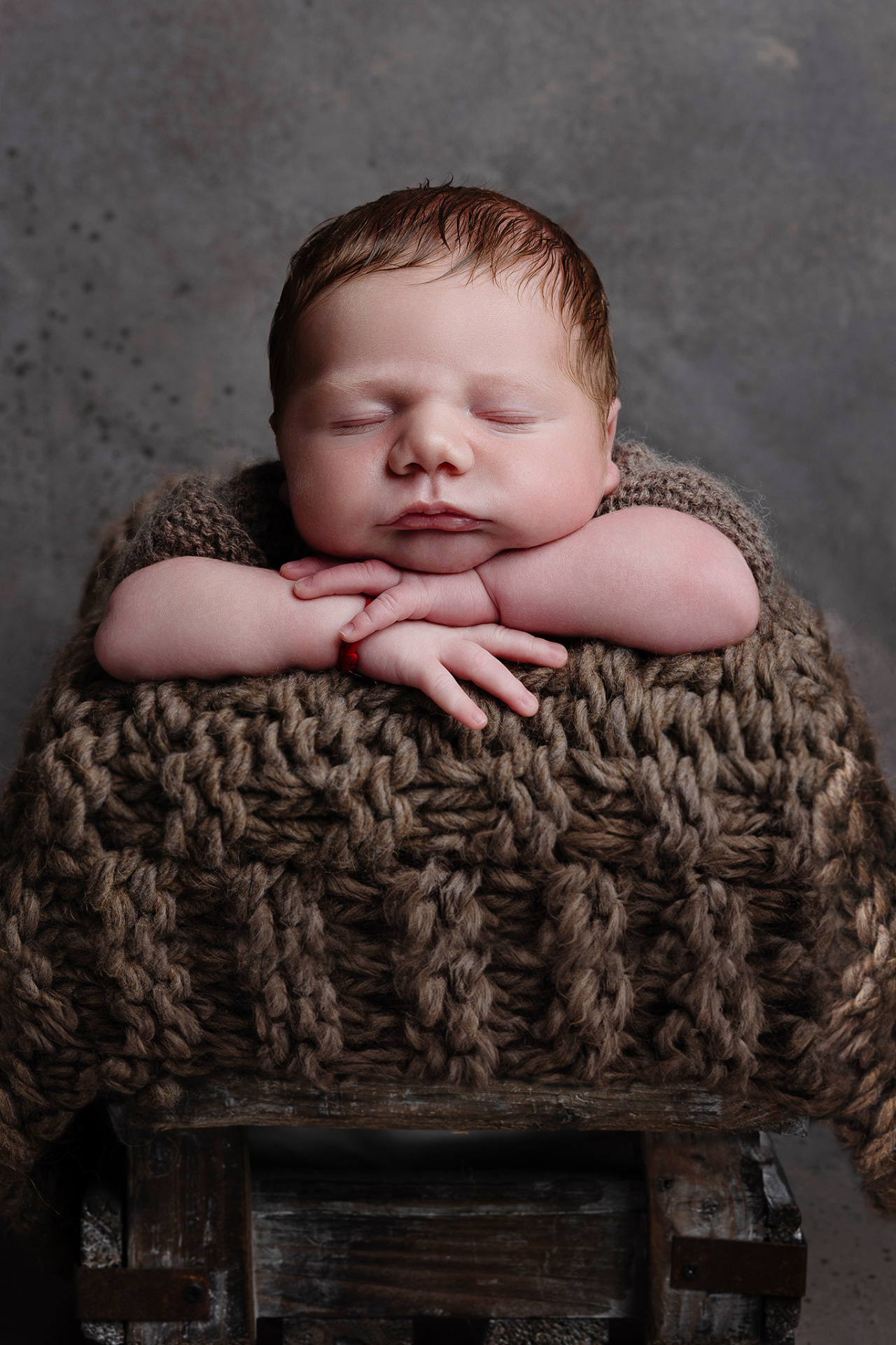 Fotografia neonatale a Bologna di Claudia Spaziani: neonato maschio addormentato in outfit marrone su coperta coordinata. Immagine che esalta serenità e dolcezza.