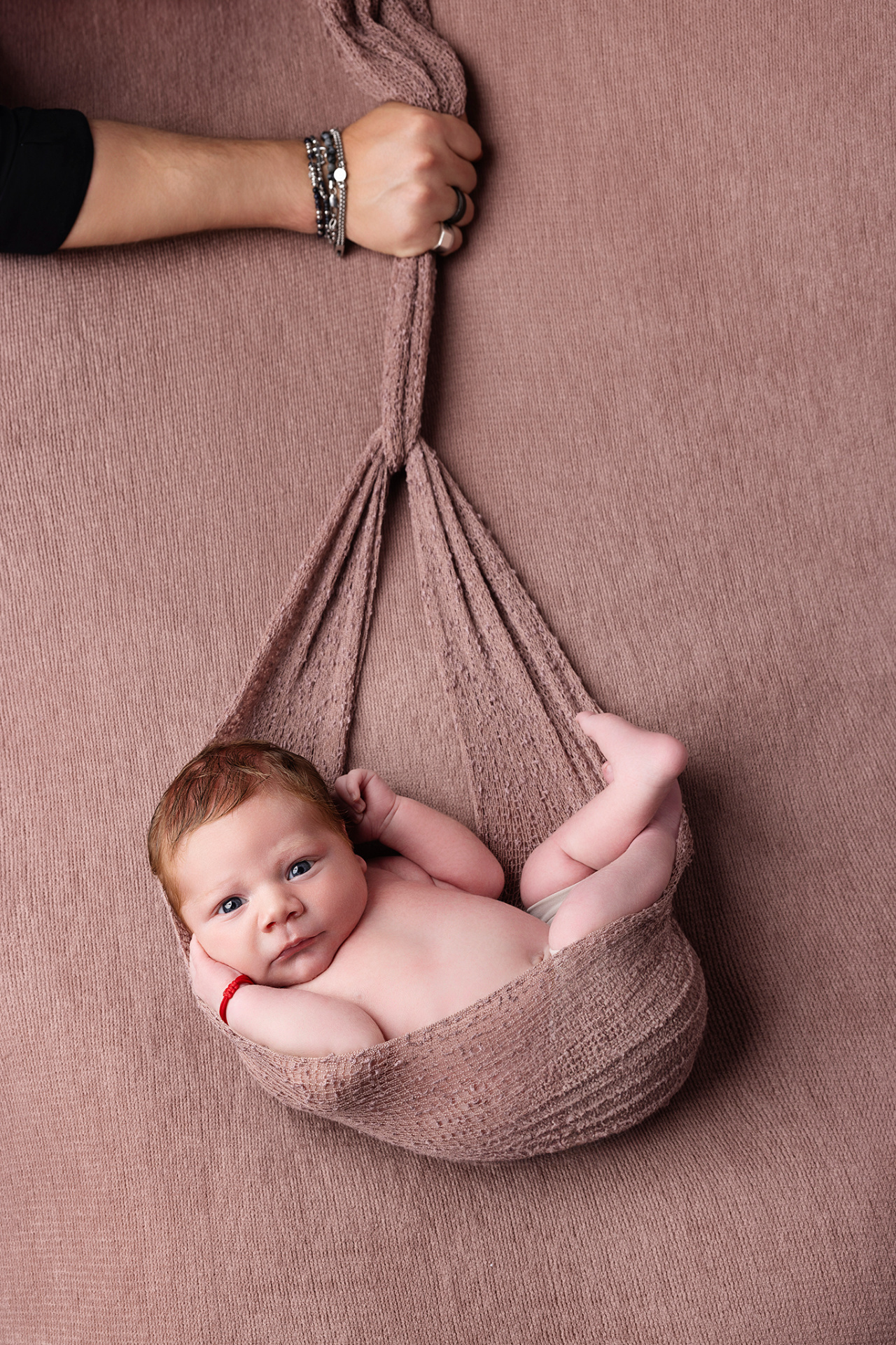 Ritratto creativo di neonato maschio posato in fascia rosa sospesa, fotografato nello studio di Claudia Spaziani a Bologna. Immagine artistica che esalta delicatezza e protezione.