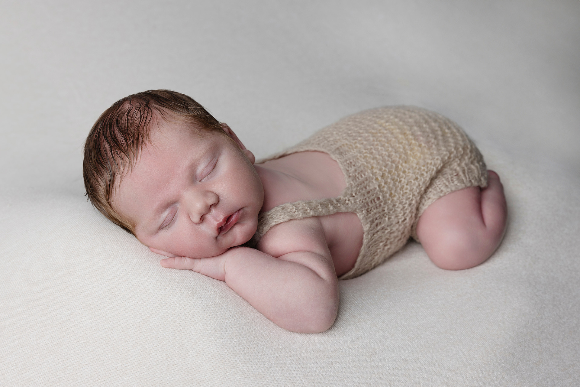 Ritratto di neonato maschio addormentato in tutina beige, posato su superficie chiara nello studio fotografico di Claudia Spaziani a Bologna. Immagine serena e delicata che esalta innocenza e tranquillità.