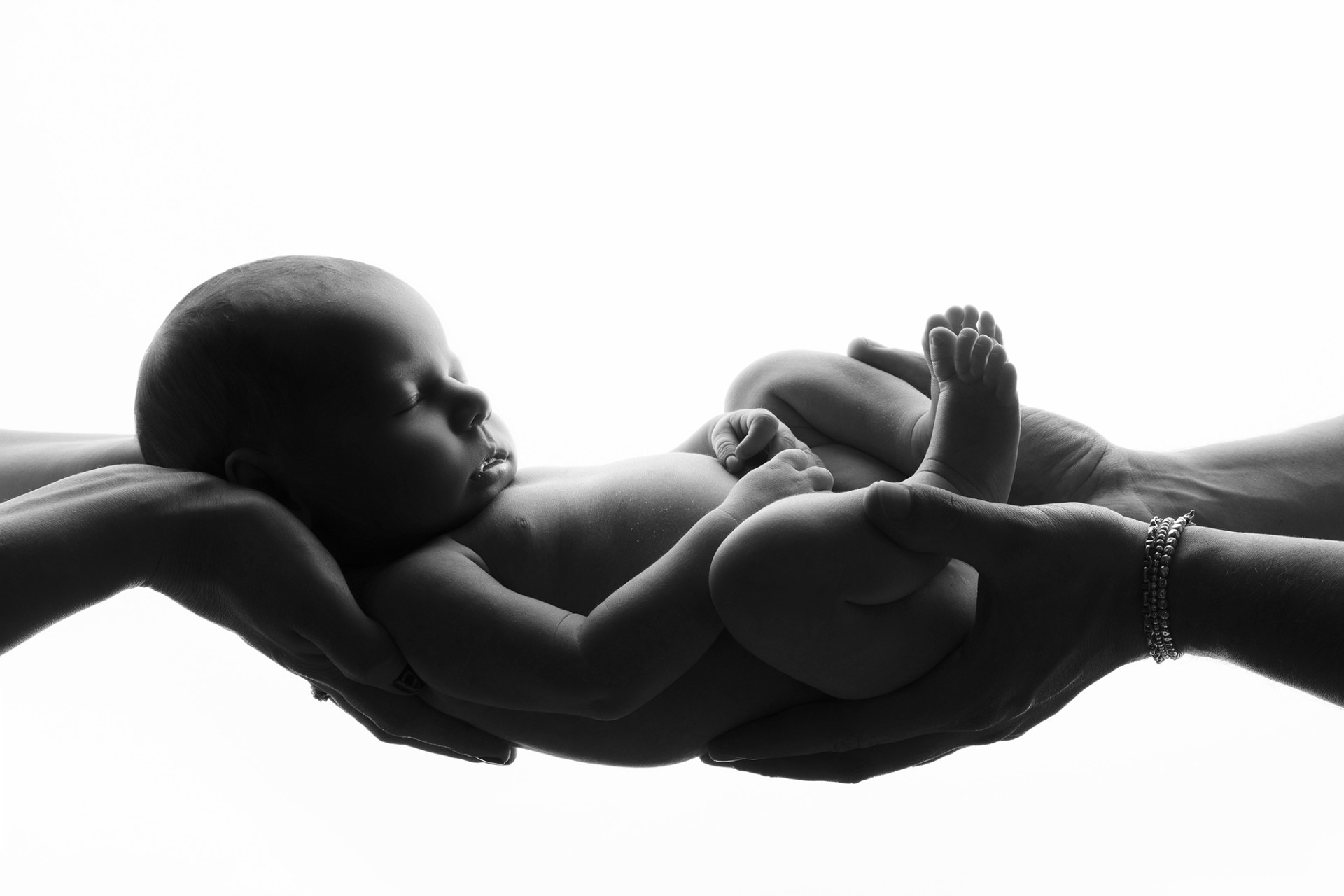 Fotografia artistica in bianco e nero di neonata addormentata sorretta da mani adulte, scattata nello studio di Claudia Spaziani a Bologna. Immagine simbolica di protezione e cura.