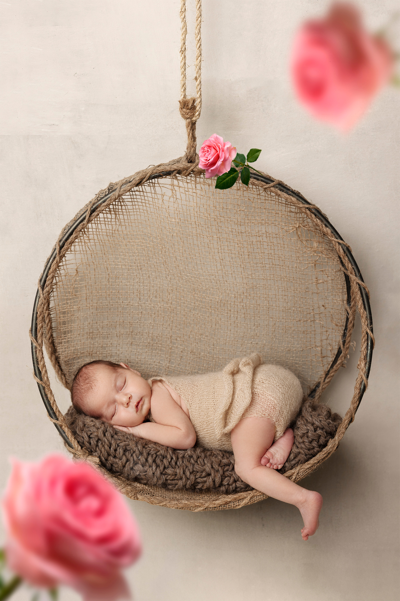 Fotografia artistica di neonata in cesta sospesa con outfit beige e rose rosa, scattata da Claudia Spaziani fotografa a Bologna. Immagine delicata e poetica che celebra nascita e innocenza.