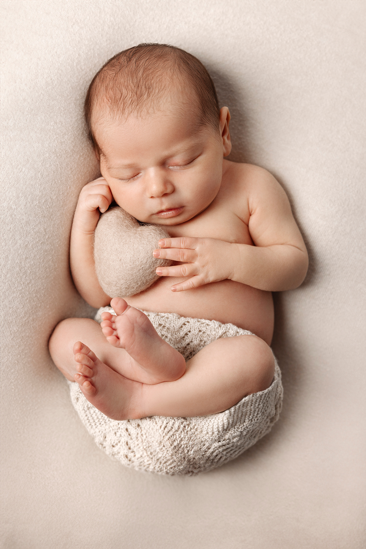 Ritratto di neonata addormentata con cuscino a forma di cuore, fotografata nello studio di Claudia Spaziani a Bologna. Immagine simbolica che esalta amore e tenerezza.