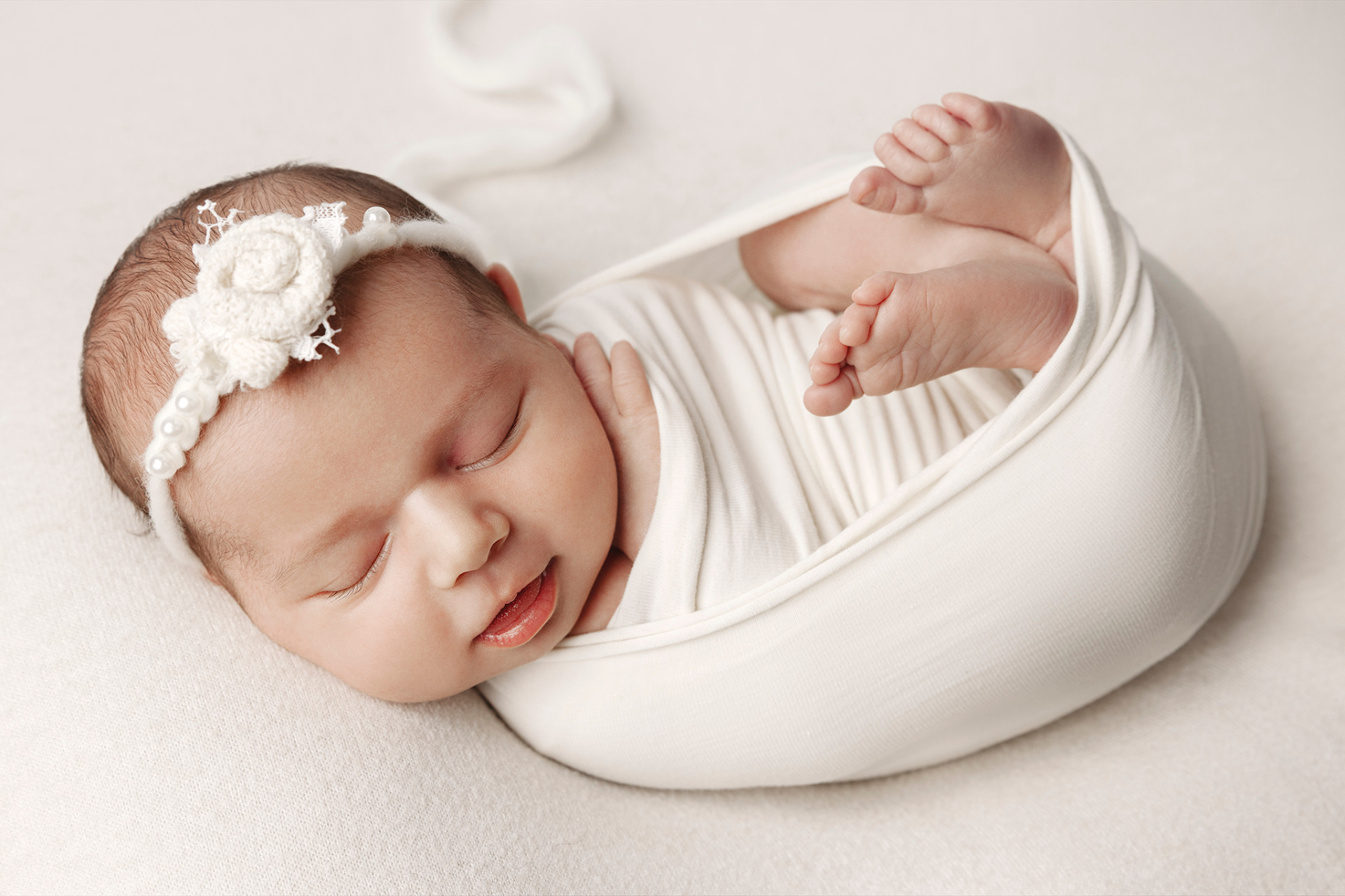 Ritratto di neonata addormentata avvolta in coperta bianca con cerchietto floreale, realizzato nello studio fotografico di Claudia Spaziani a Bologna. Immagine elegante e serena.