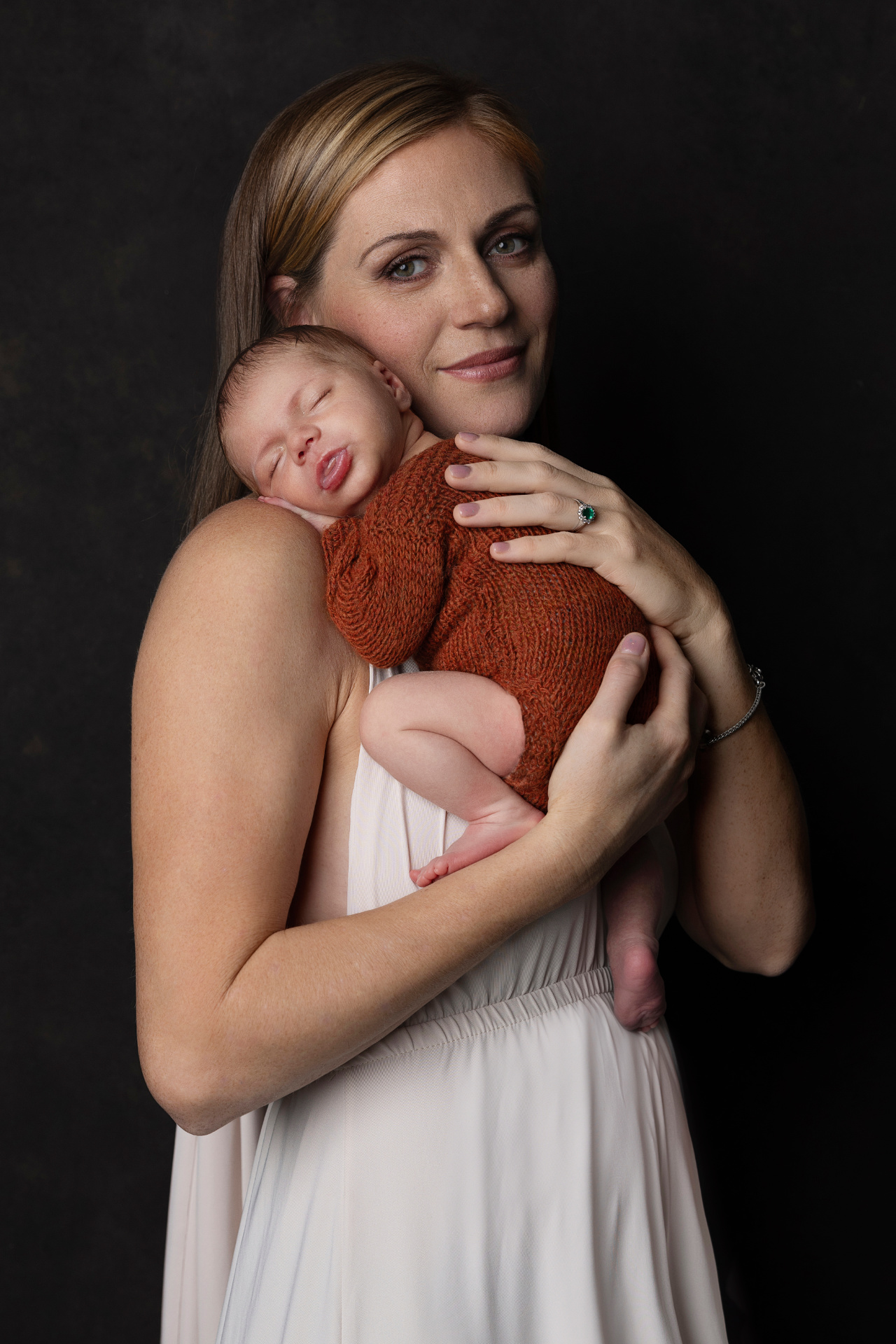 Foto intima di madre che culla neonato maschio in abito marrone, scattata da Claudia Spaziani fotografa a Bologna. Immagine elegante e affettuosa.