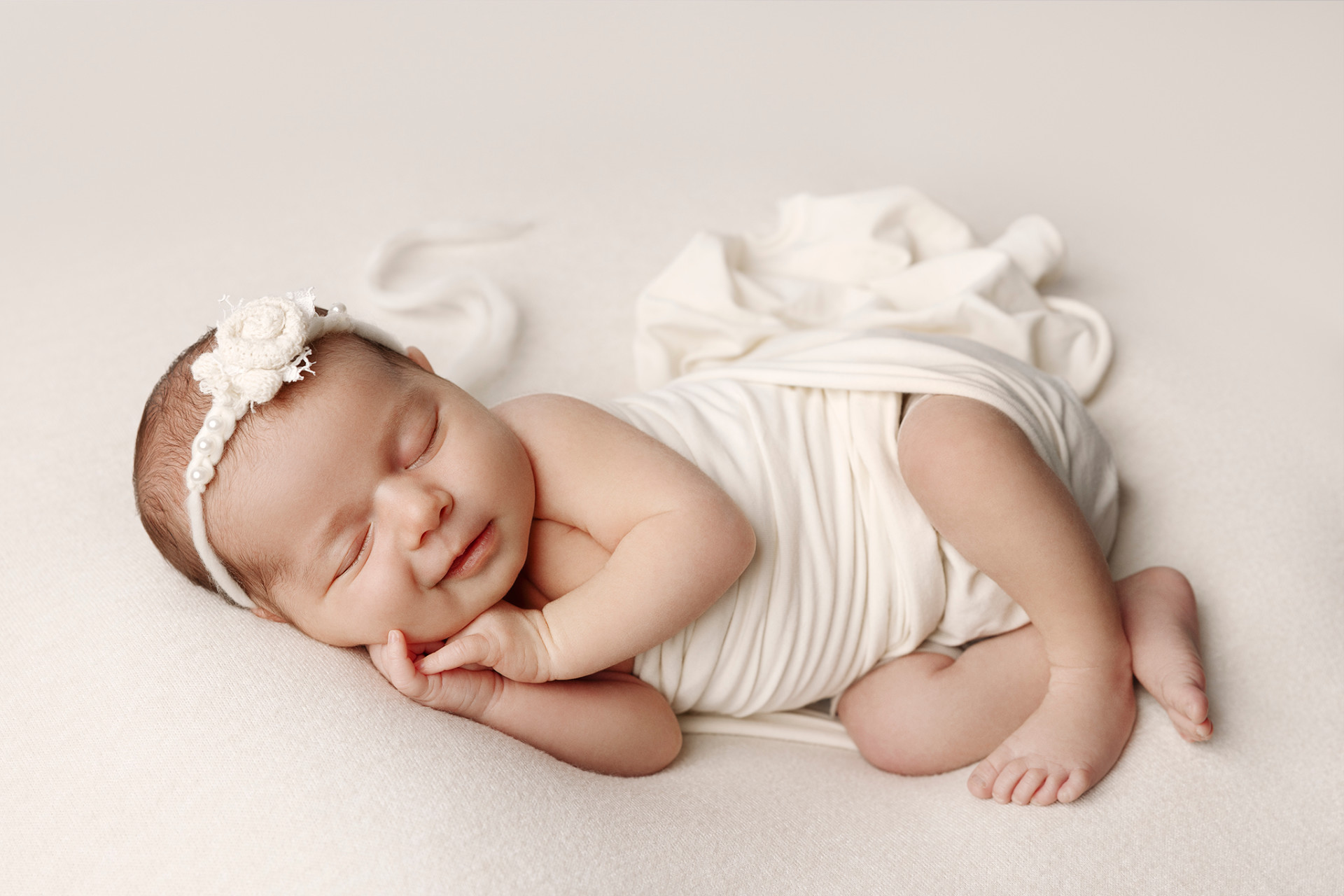 Ritratto di neonata addormentata avvolta in fascia bianca, con delicato cerchietto floreale, fotografata nello studio di Claudia Spaziani a Bologna. Immagine minimalista e serena che esalta innocenza e dolcezza.
