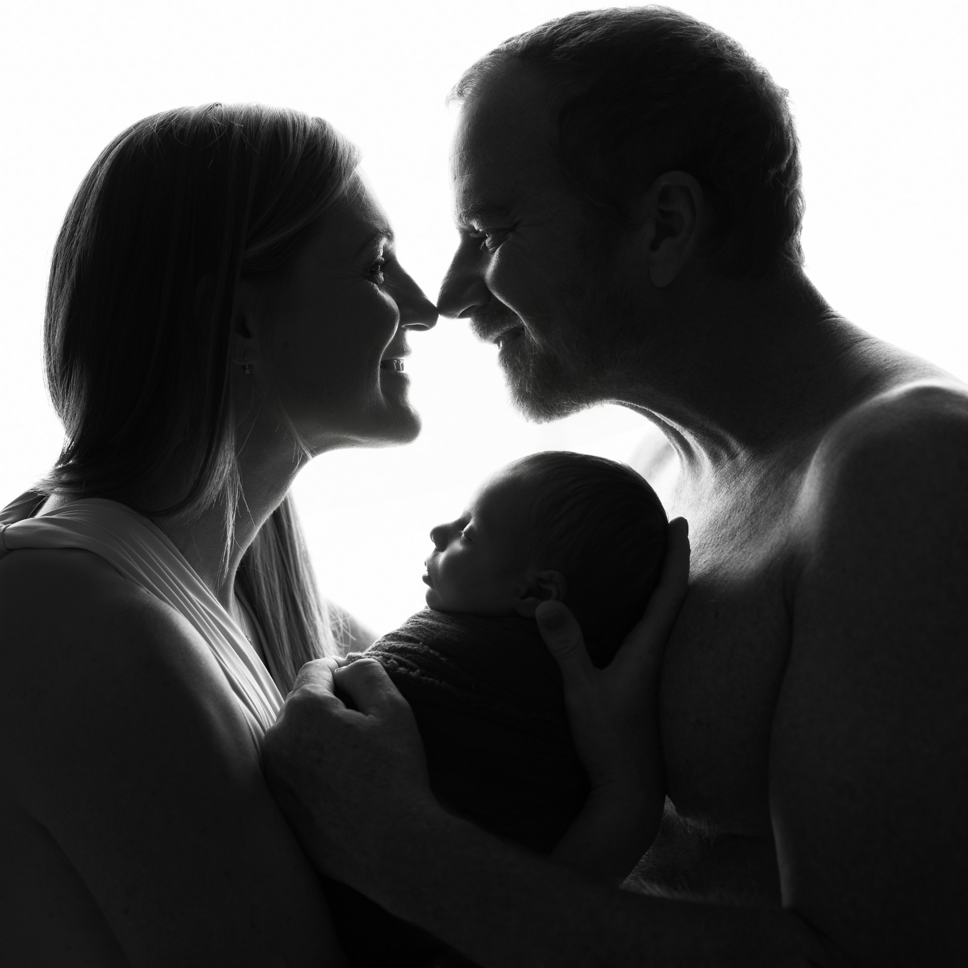 Ritratto in silhouette di genitori con neonato maschio avvolto in coperta, scattato nello studio di Claudia Spaziani a Bologna. Immagine che celebra amore e protezione.