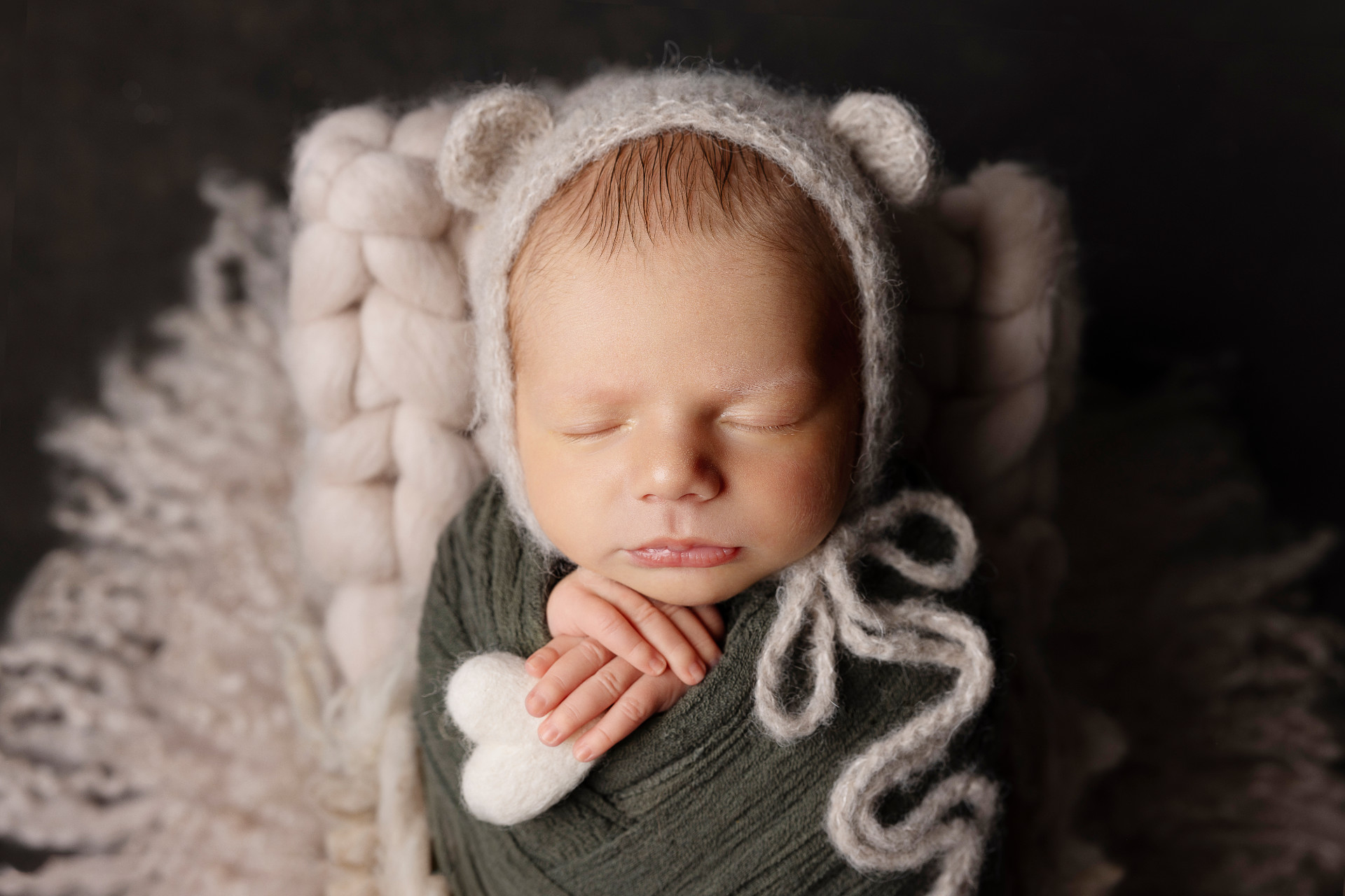 Ritratto di neonato maschio avvolto in fascia verde con cuore e fiocco decorativi, cappellino con orecchie da orsetto, fotografato nello studio di Claudia Spaziani a Bologna. Immagine dolce e accogliente.