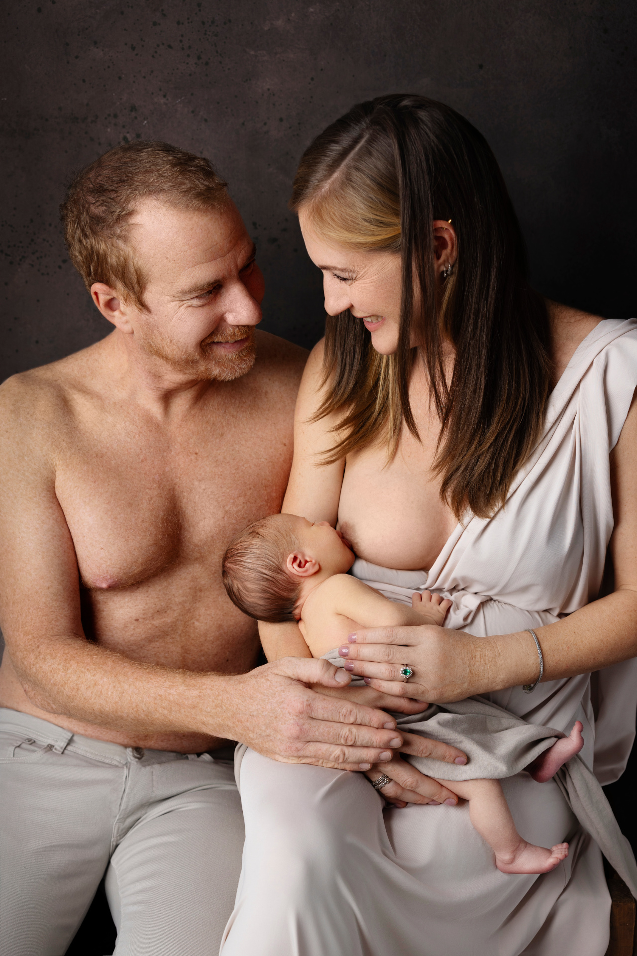 Foto intima di madre che allatta neonato maschio, con padre accanto, scattata nello studio fotografico di Claudia Spaziani a Bologna. Immagine che celebra amore e legame familiare.