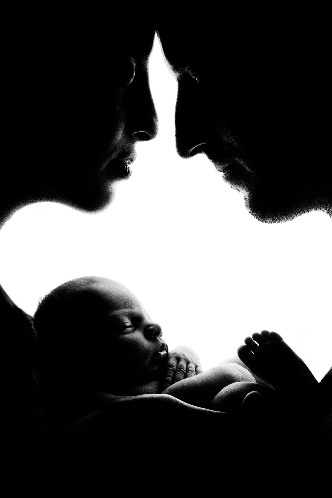 Fotografia in bianco e nero in silhouette di genitori con neonata addormentata, realizzata da Claudia Spaziani fotografa a Bologna. Immagine artistica che esprime amore e protezione.
