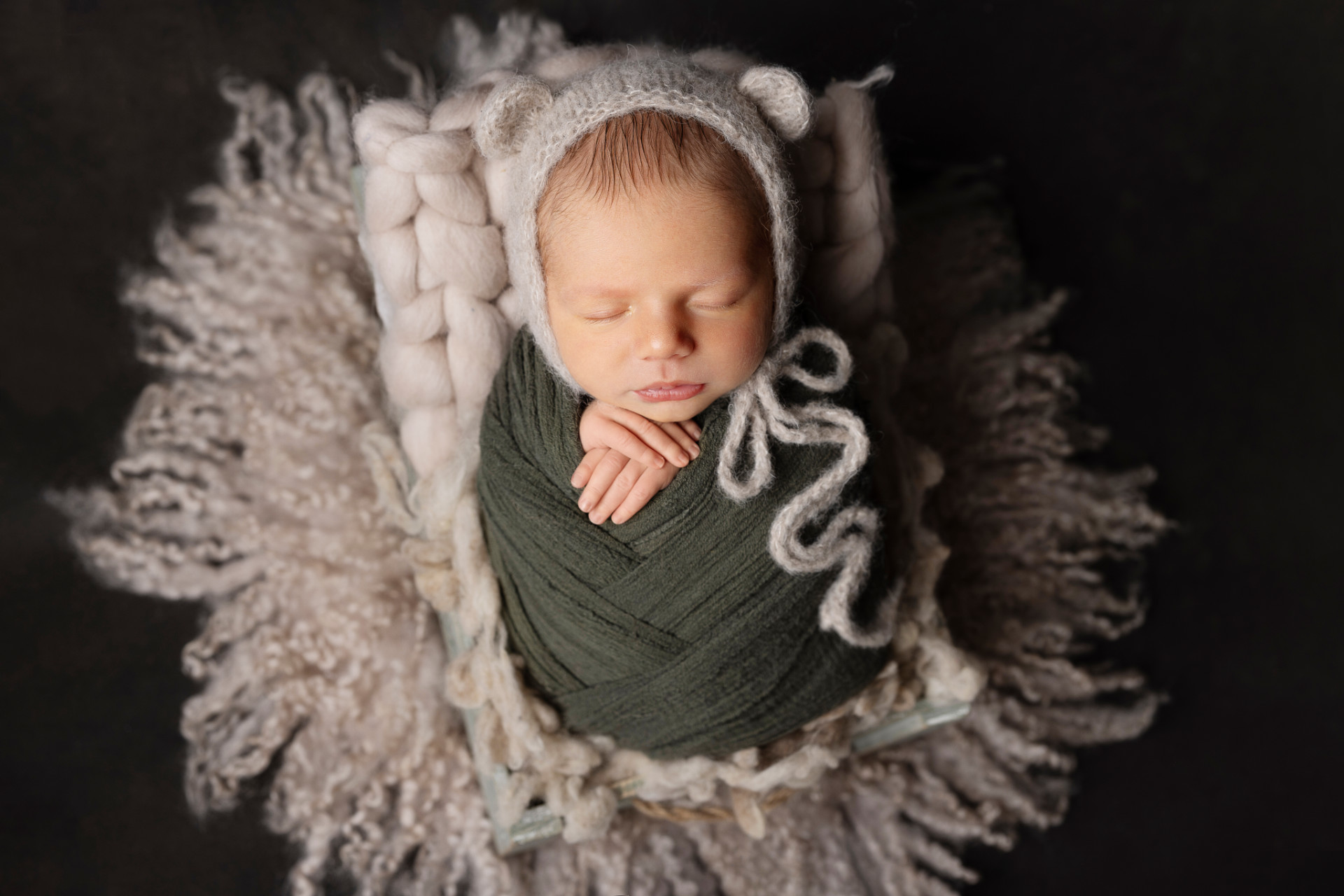 Ritratto di neonato maschio addormentato in fascia verde con cappellino a orecchie da orsetto, fotografato da Claudia Spaziani a Bologna. Immagine dolce e fiabesca.