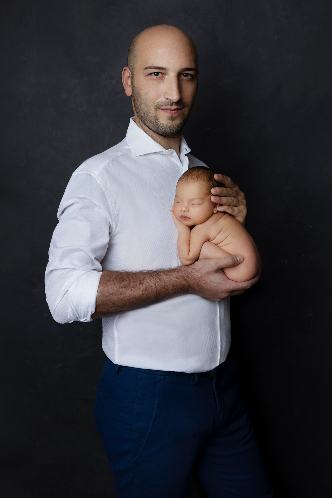 Foto di padre con neonata addormentata in braccio, scattata nello studio di Claudia Spaziani a Bologna. Immagine elegante e professionale che celebra il legame familiare.