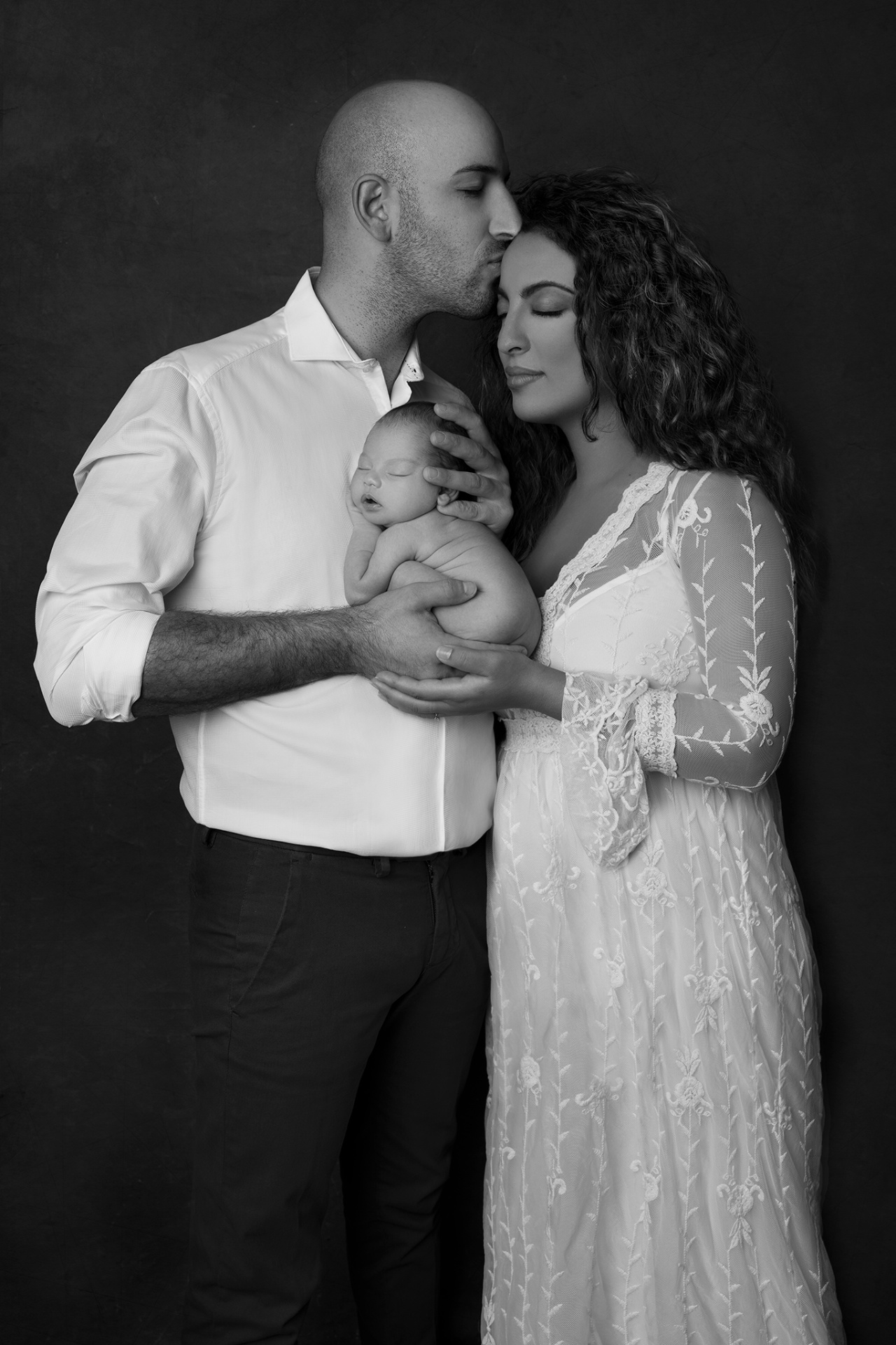 Ritratto di famiglia in bianco e nero con neonata addormentata, fotografato da Claudia Spaziani a Bologna. Immagine intima che esalta amore e connessione.