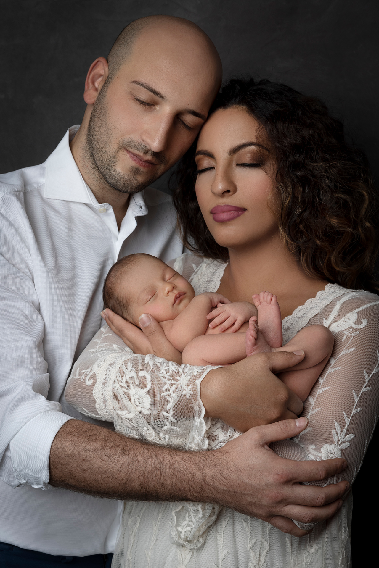 Foto di famiglia con neonata addormentata, scattata nello studio fotografico di Claudia Spaziani a Bologna. Immagine elegante e affettuosa che celebra la nascita.
