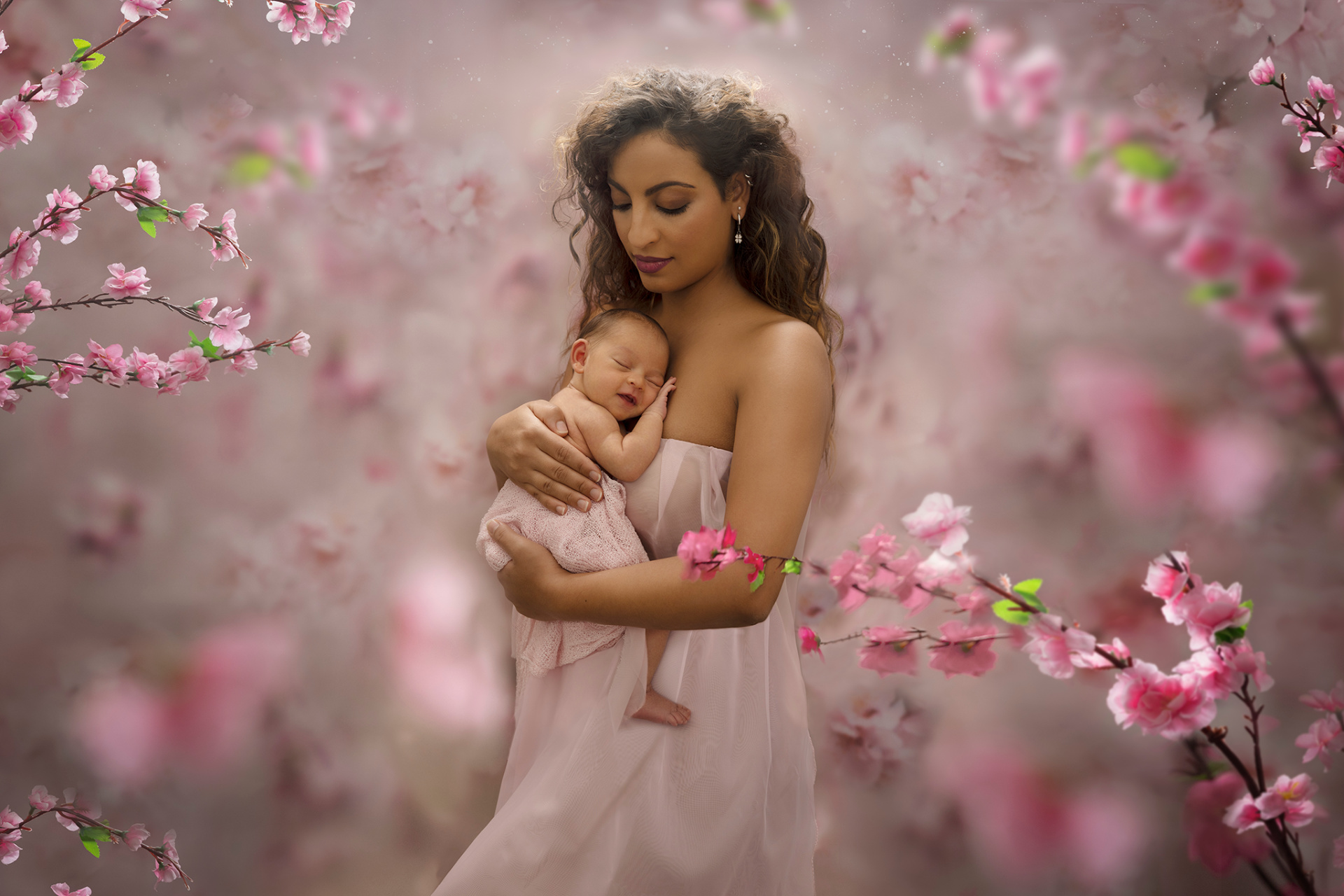Ritratto di madre con neonata addormentata tra fiori di ciliegio rosa, scattato da Claudia Spaziani fotografa a Bologna. Immagine poetica e primaverile che celebra maternità e tenerezza.