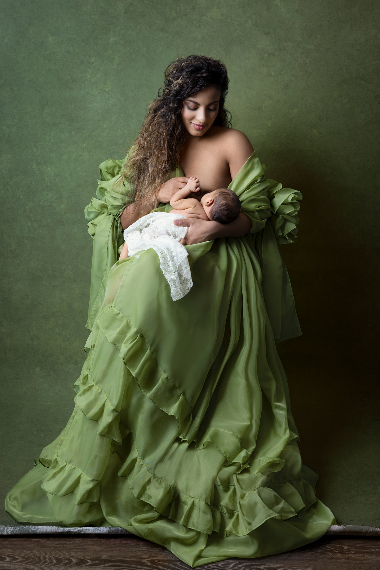 Ritratto di madre in abito verde che allatta la neonata vestita di pizzo bianco, scattato da Claudia Spaziani fotografa a Bologna. Fotografia elegante e naturale.