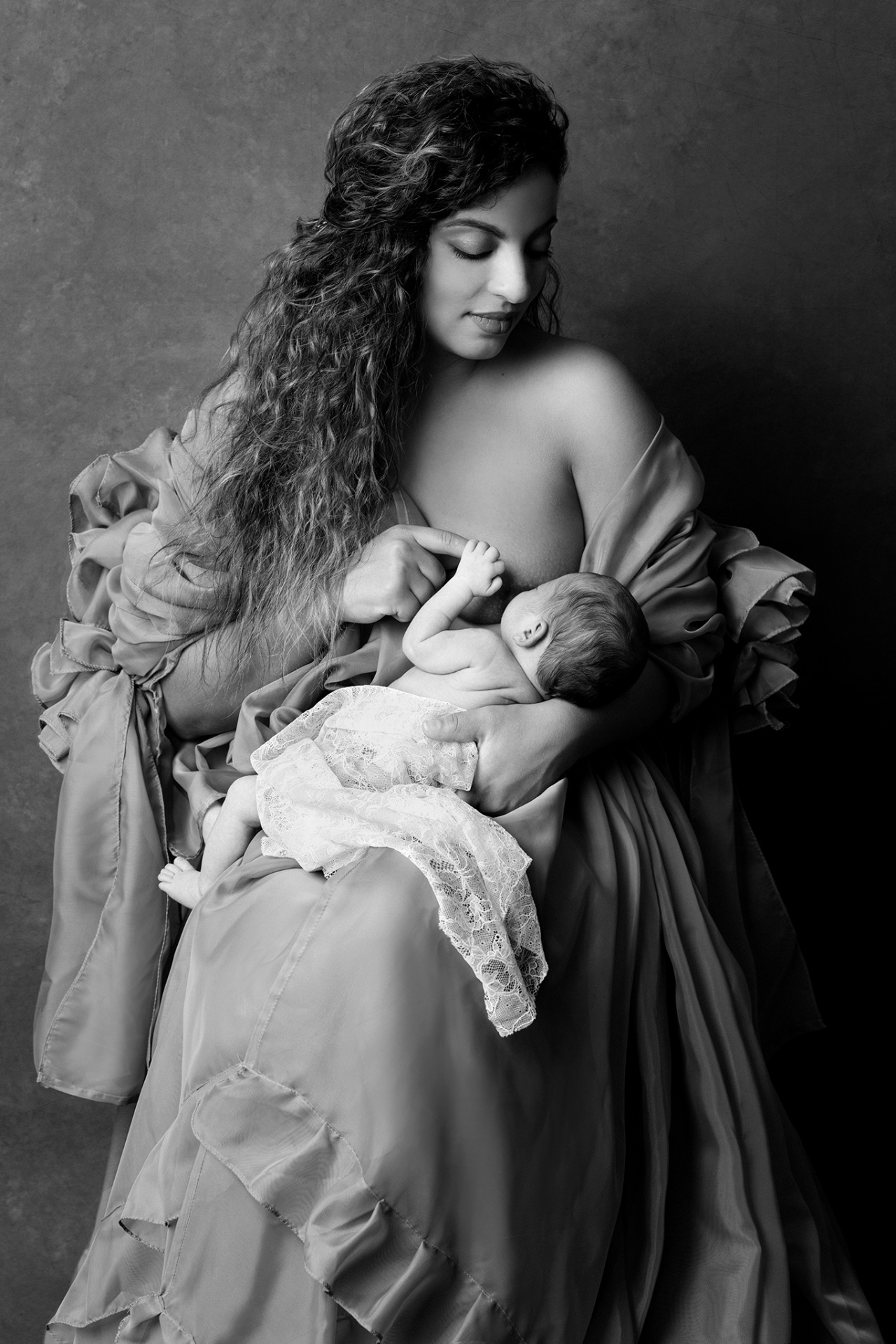 Fotografia artistica in bianco e nero di madre che allatta la neonata, realizzata nello studio di Claudia Spaziani a Bologna. Immagine intima e senza tempo che celebra maternità e legame.