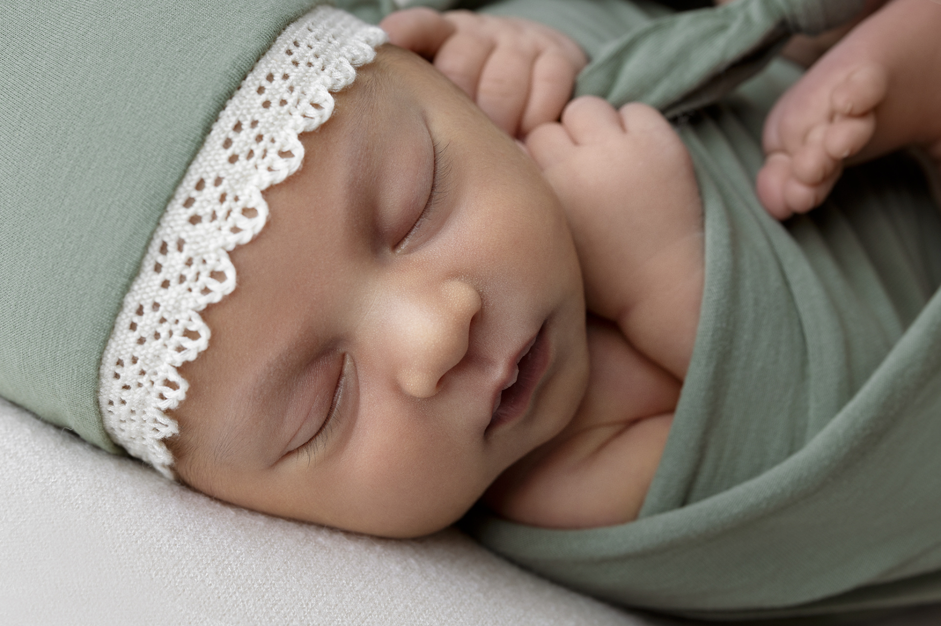 Primo piano di neonata addormentata in fascia verde con cappellino coordinato, fotografata nello studio di Claudia Spaziani a Bologna. Immagine delicata e rassicurante.