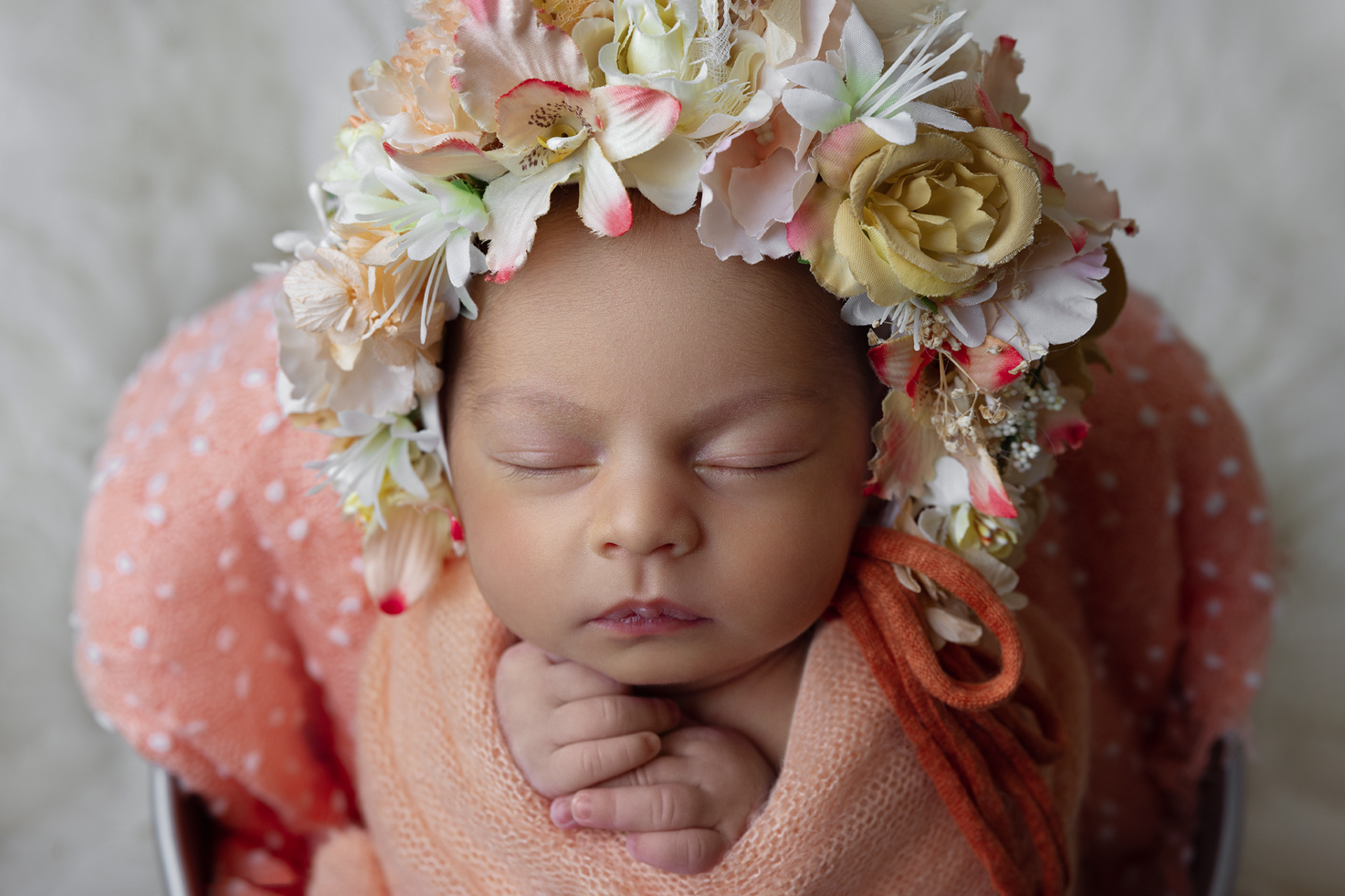 Ritratto di neonata avvolta in coperta pesca a pois, con cerchietto floreale multicolore, scattato nello studio fotografico di Claudia Spaziani a Bologna. Fotografia che esalta innocenza e delicatezza.
