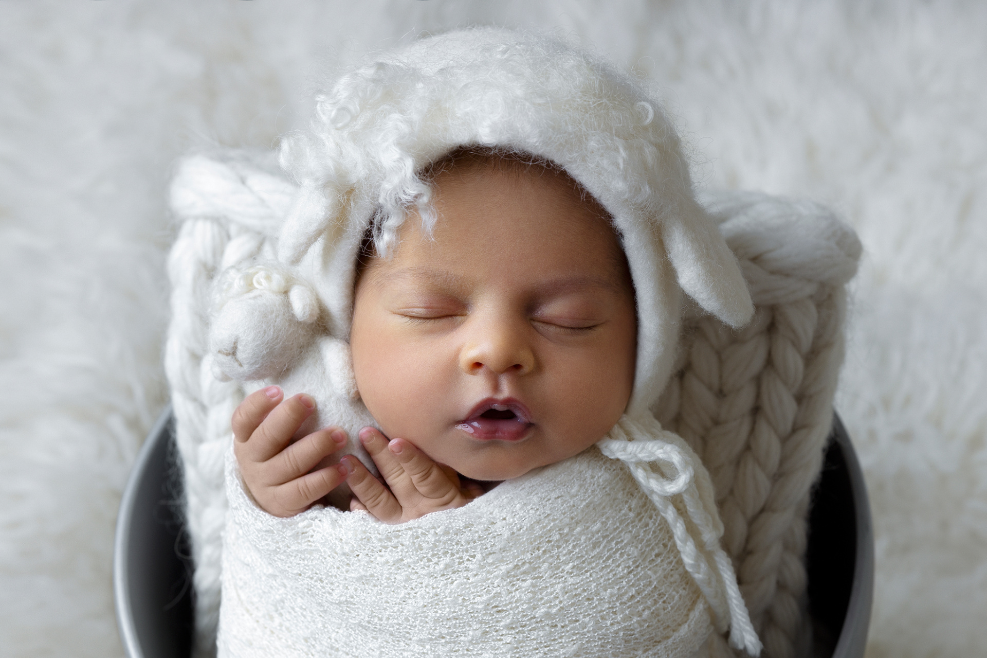 Ritratto neonatale a Bologna di Claudia Spaziani: neonata avvolta in coperta bianca con cappellino a orecchie di agnello, che stringe un piccolo pupazzo. Fotografia dolce e accogliente.