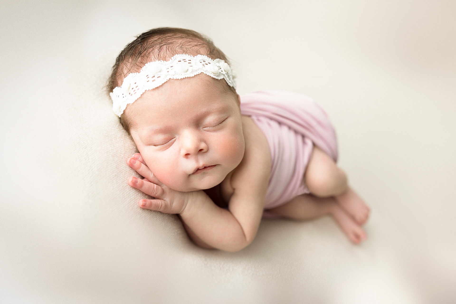 Ritratto neonatale a Bologna di Claudia Spaziani: neonato avvolto in fascia rosa con cerchietto floreale, addormentato serenamente su superficie chiara. Fotografia che esalta innocenza e dolcezza.