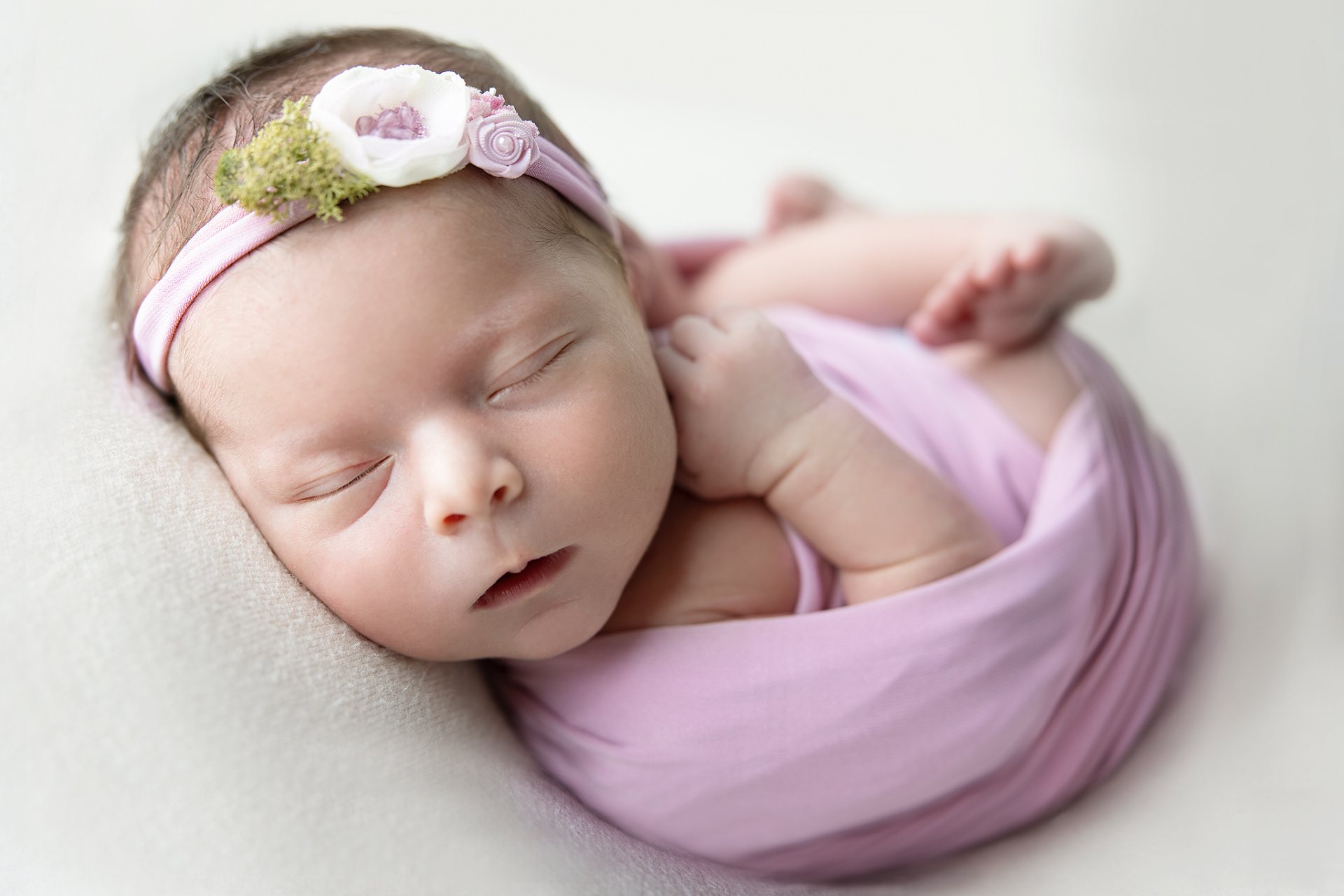 Foto Newborn con neonato addormentato, realizzata da Claudia Spaziani fotografa a Bologna. Genitori in abiti bianchi sostengono il bambino con tenerezza, in un ritratto elegante e senza tempo.