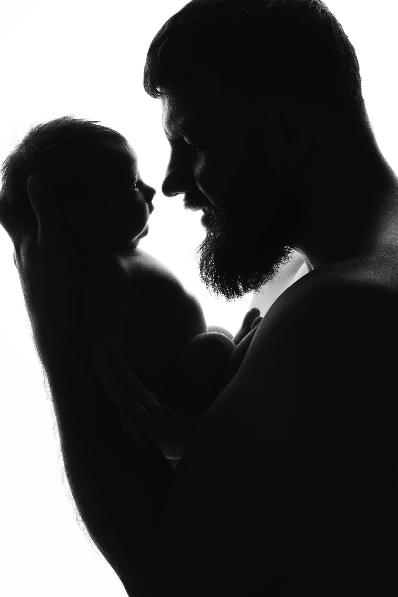Fotografia newborn a Bologna realizzata da Claudia Spaziani: silhouette in bianco e nero di papà con barba che tiene il neonato.