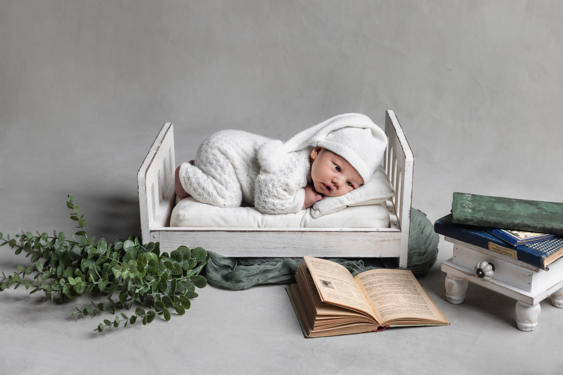 Servizio fotografico newborn a Bologna di Claudia Spaziani: neonato in outfit da coniglietto su lettino bianco con libri e piante decorative.