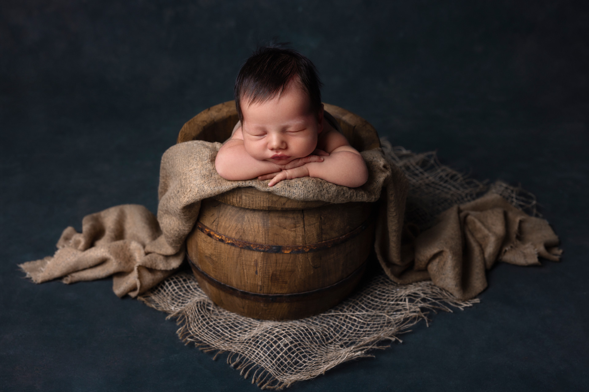 Servizio fotografico newborn a Bologna di Claudia Spaziani: neonato che dorme in barile rustico con tessuti naturali e luce soffusa.