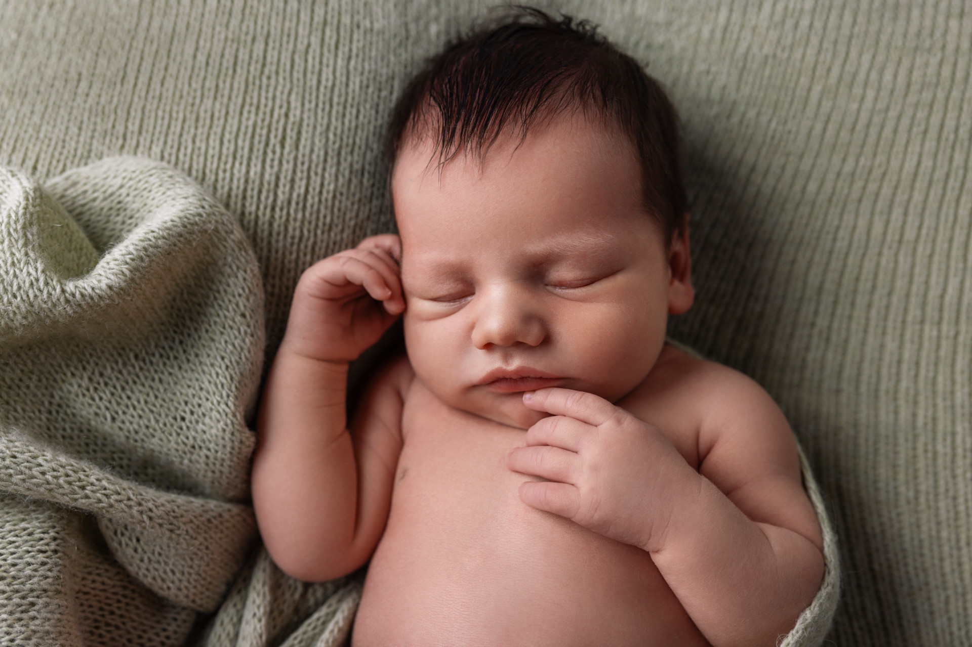 Claudia Spaziani fotografa newborn a Bologna: primo piano di neonato che dorme su coperta verde, con mano vicino al volto.