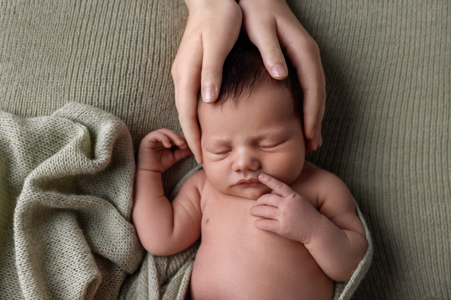 Fotografia newborn a Bologna realizzata da Claudia Spaziani: neonato che riposa su coperta verde, con la testa sorretta da mani protettive.