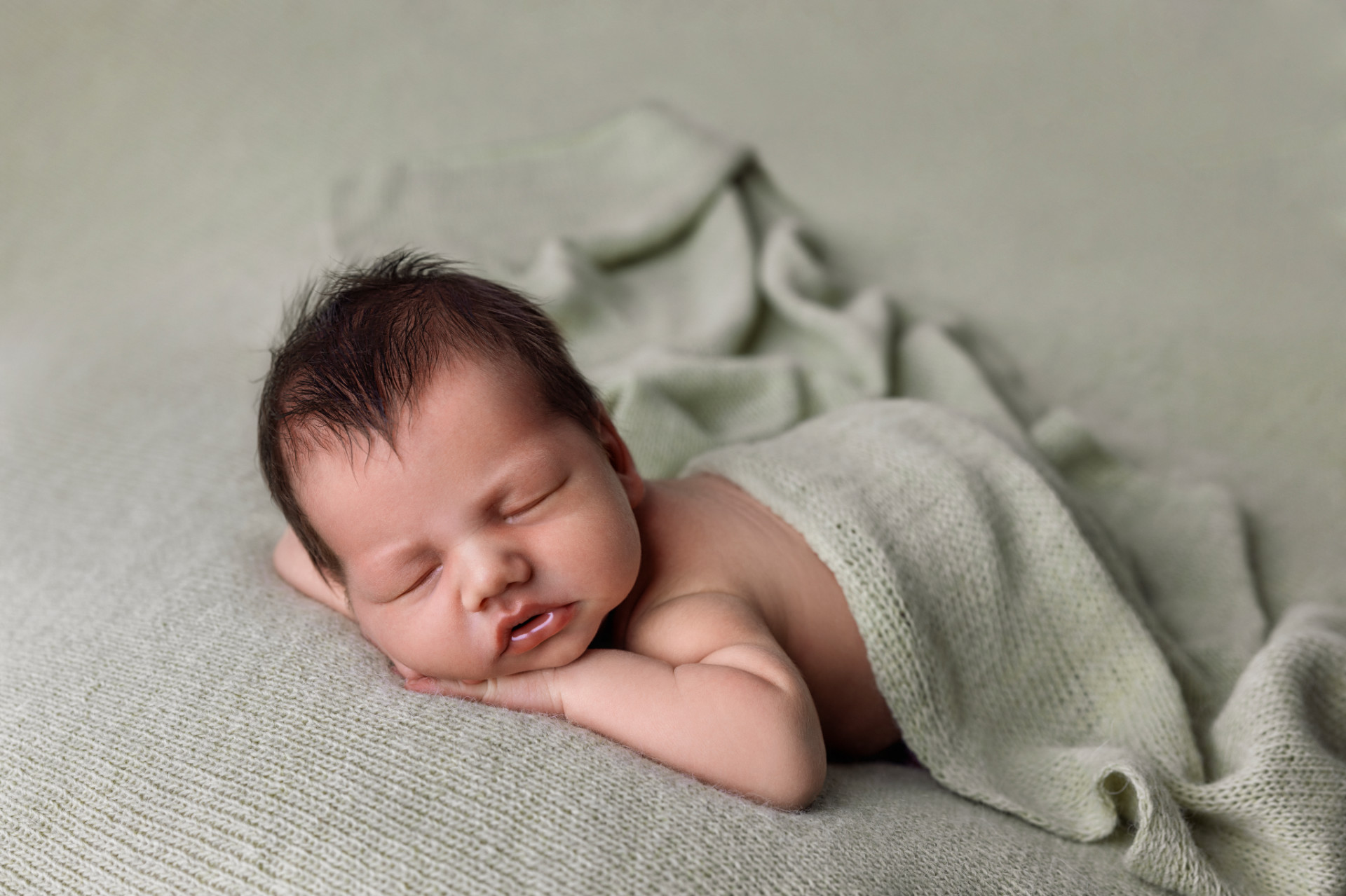Servizio fotografico newborn a Bologna realizzato da Claudia Spaziani: neonato che dorme sereno avvolto in copertina verde su sfondo morbido.