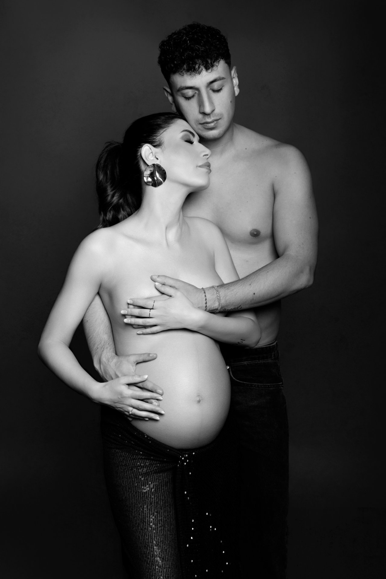 Ritratto artistico di coppia maternità in bianco e nero a Bologna realizzato da Claudia Spaziani: donna incinta abbracciata dal partner, atmosfera intima.