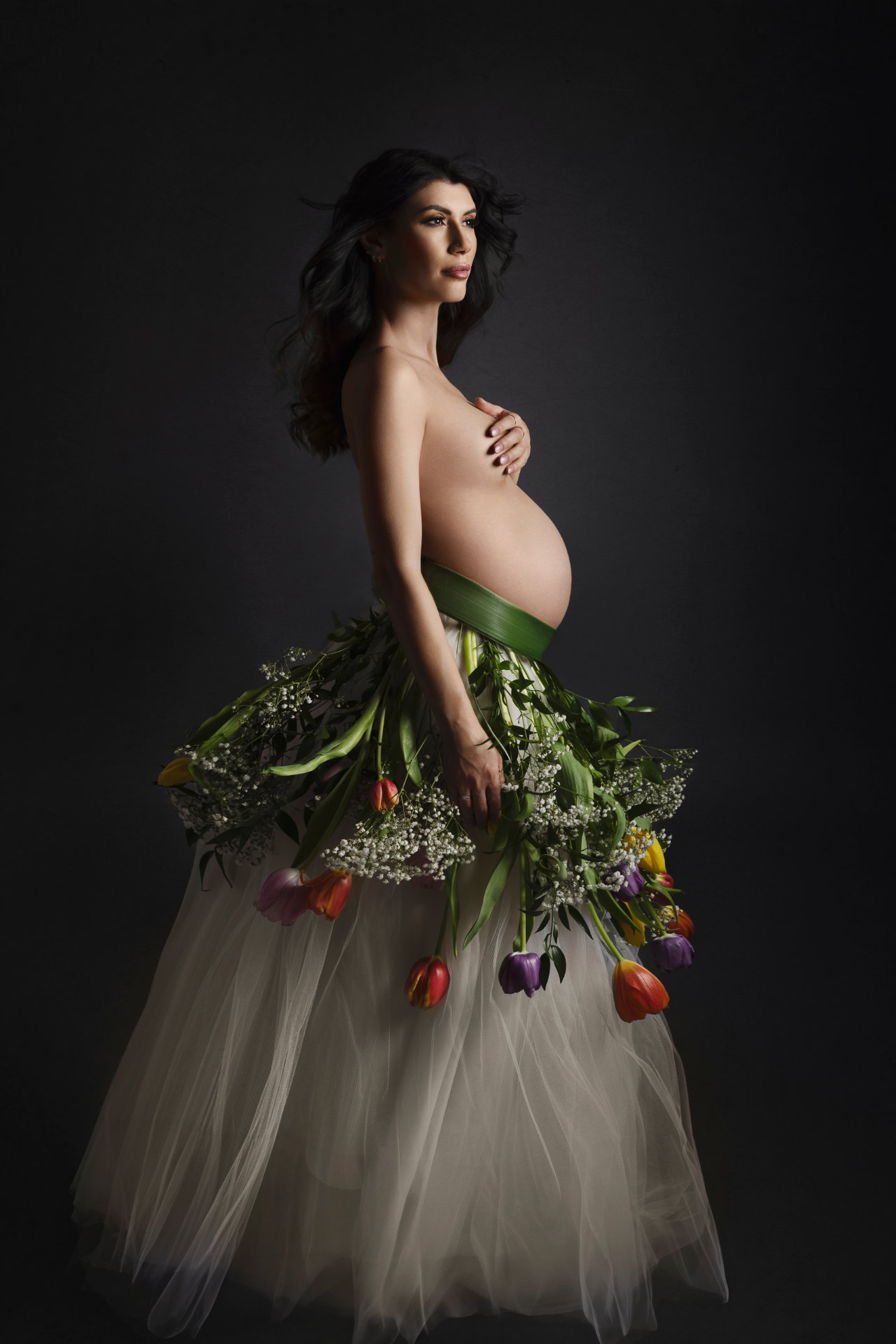Ritratto artistico di maternità a Bologna realizzato da Claudia Spaziani: donna incinta con gonna di tulle e fiori colorati, atmosfera naturale e simbolica.