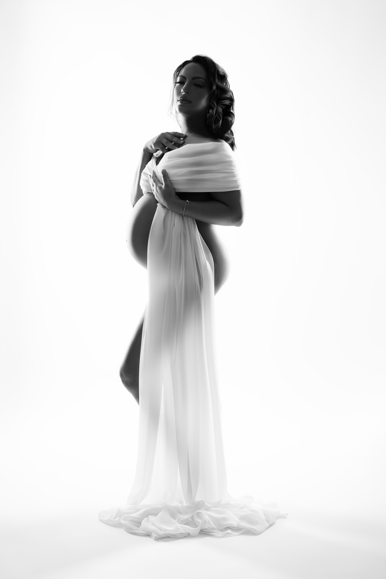 Foto maternità in bianco e nero a Bologna realizzata da Claudia Spaziani: donna incinta in tessuto trasparente, posa elegante e luce drammatica.
