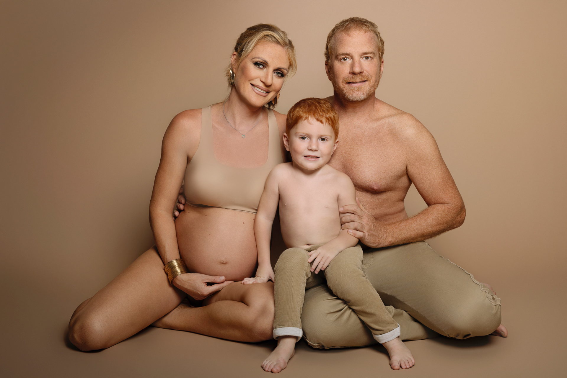 Foto di famiglia a Bologna realizzata da Claudia Spaziani: coppia con bambino e donna incinta su sfondo beige, atmosfera calda e armoniosa.