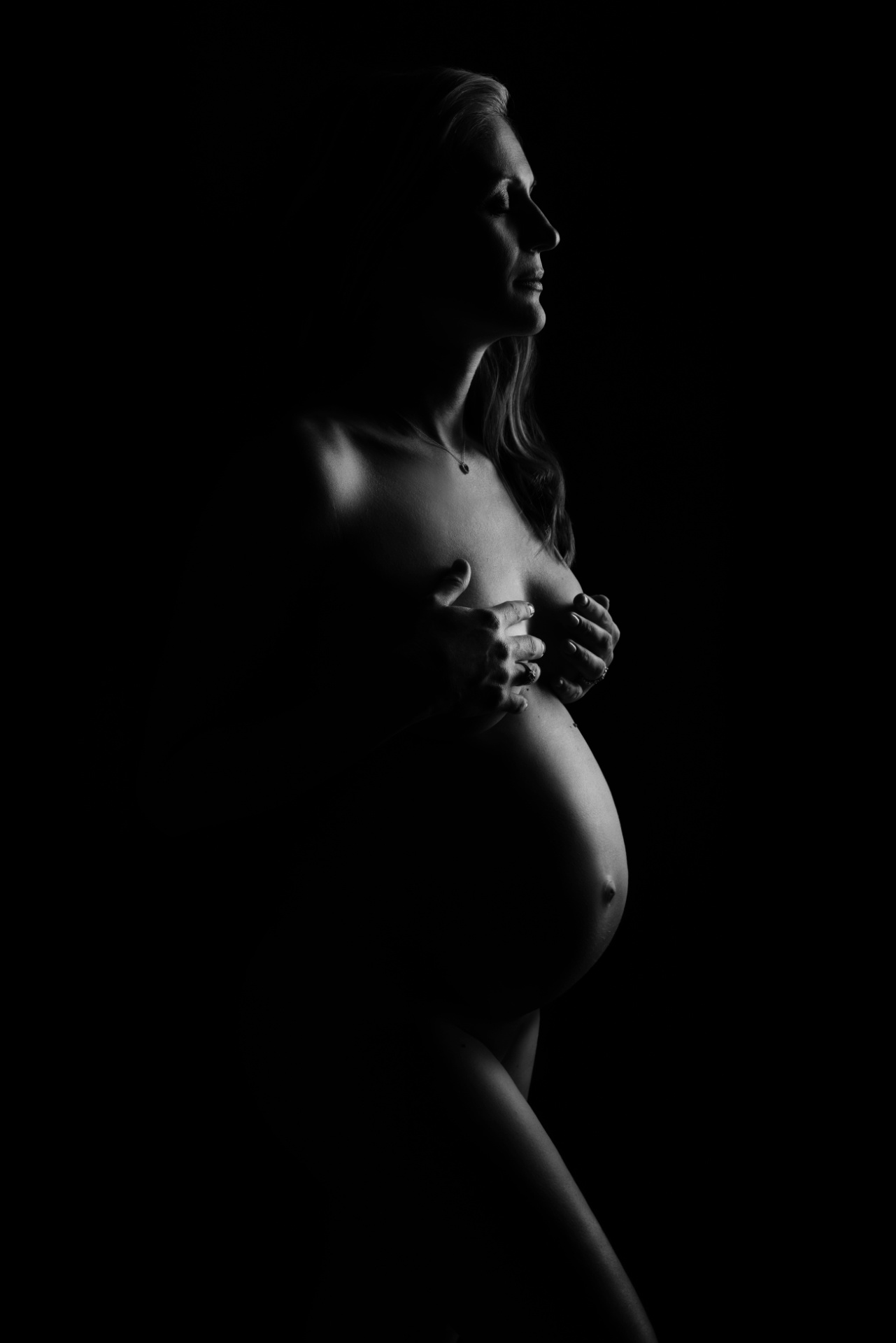 Ritratto artistico di maternità in bianco e nero a Bologna firmato Claudia Spaziani: donna incinta in profilo con luce drammatica, atmosfera intima e potente.