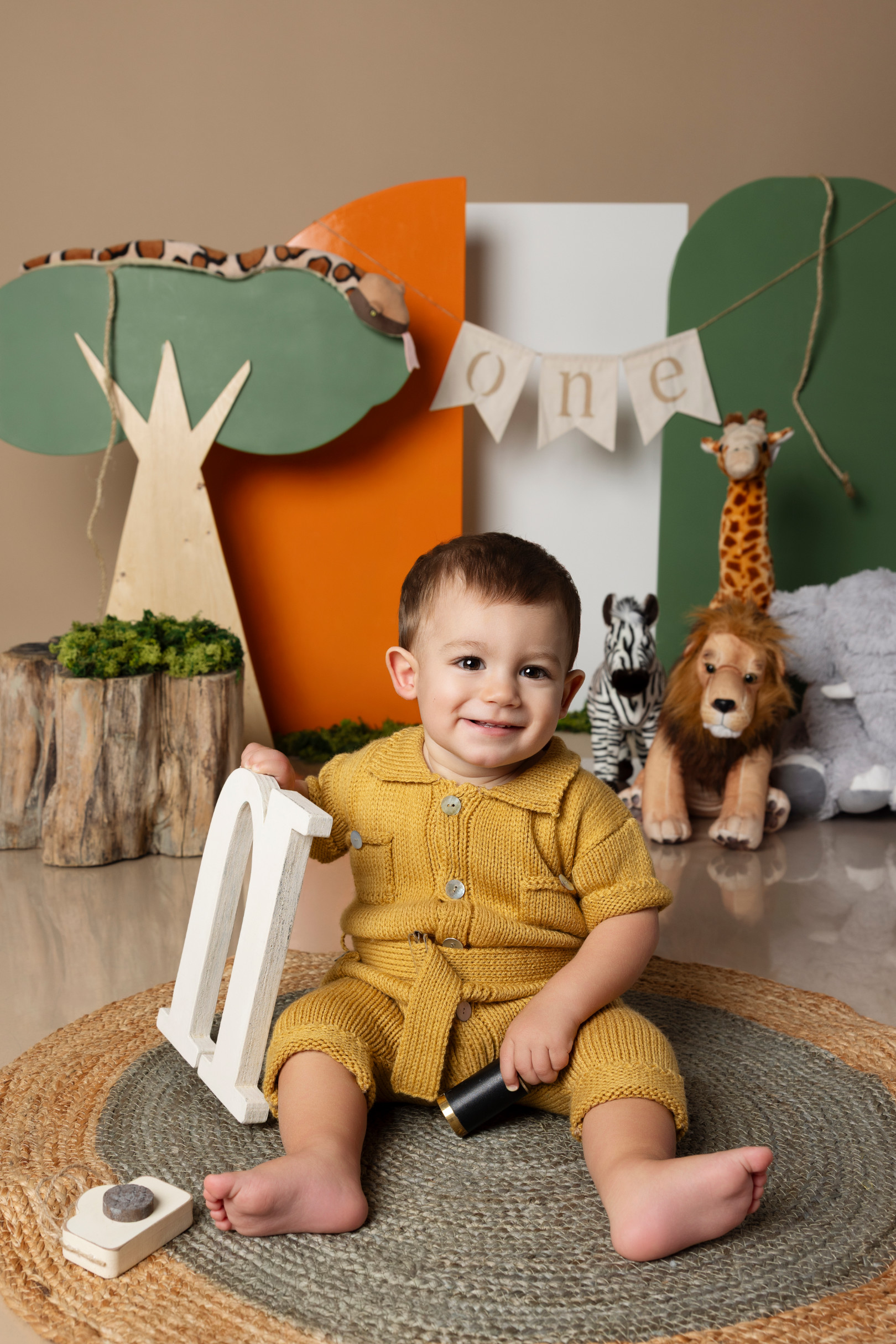 Bambino sorridente accanto alla lettera di legno “N” tra giraffa e leone di peluche — smash cake a tema safari a Bologna.
