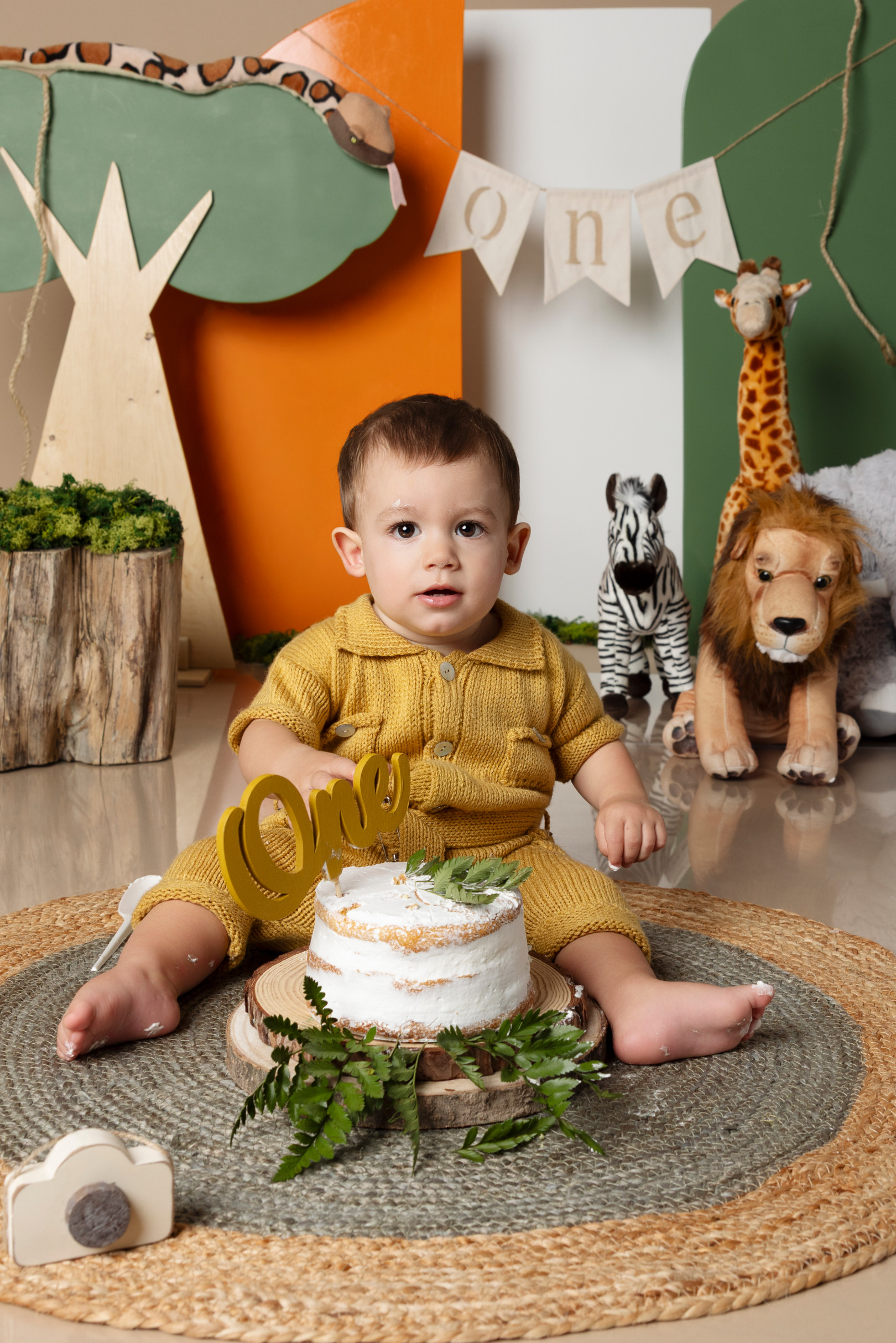 Bambino seduto dietro la torta bianca decorata con felci e topper “One” — smash cake a tema safari a Bologna.