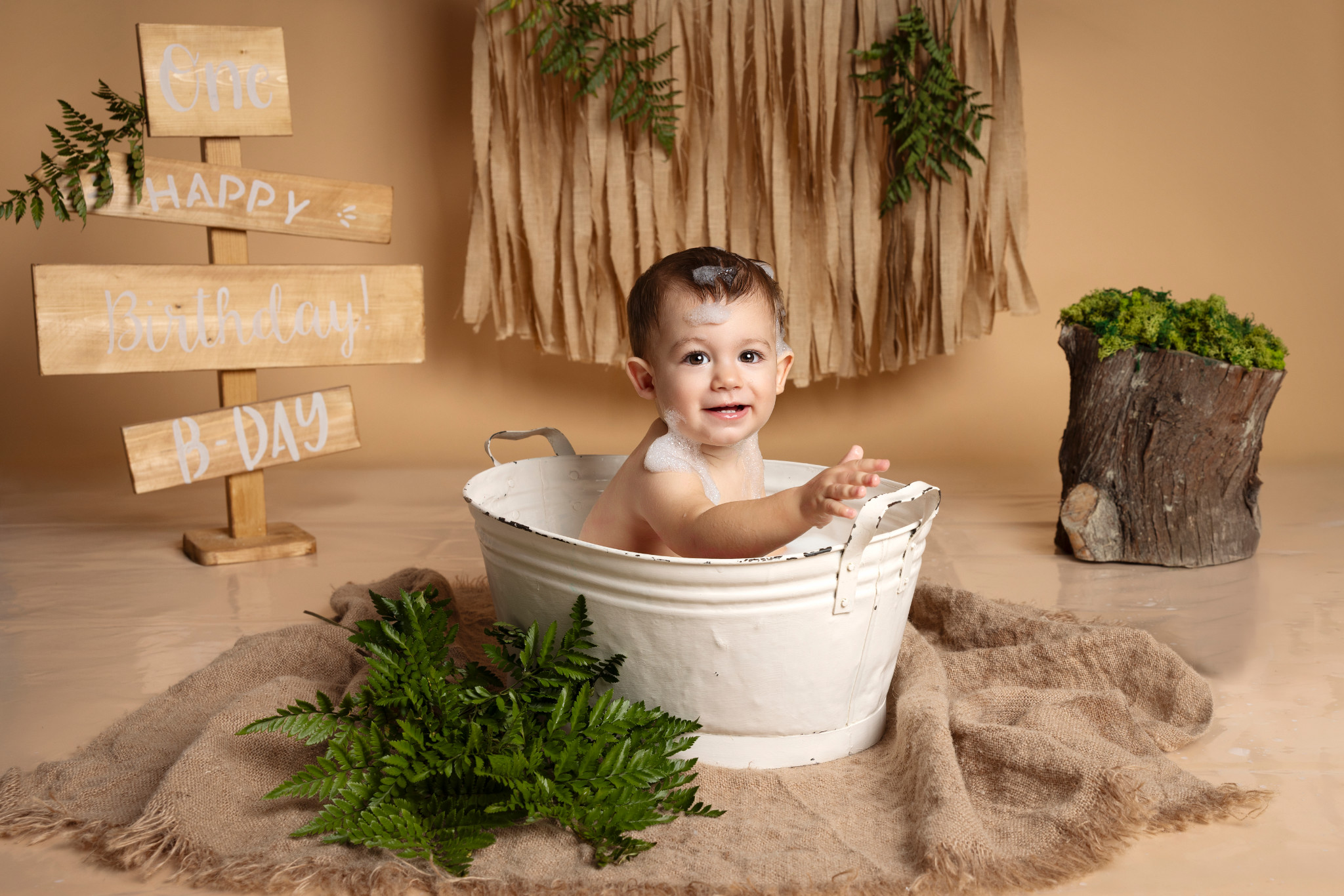 Bambino nella vasca allunga la mano verso i cartelli “Happy Birthday” — set splash boho naturale a Bologna.