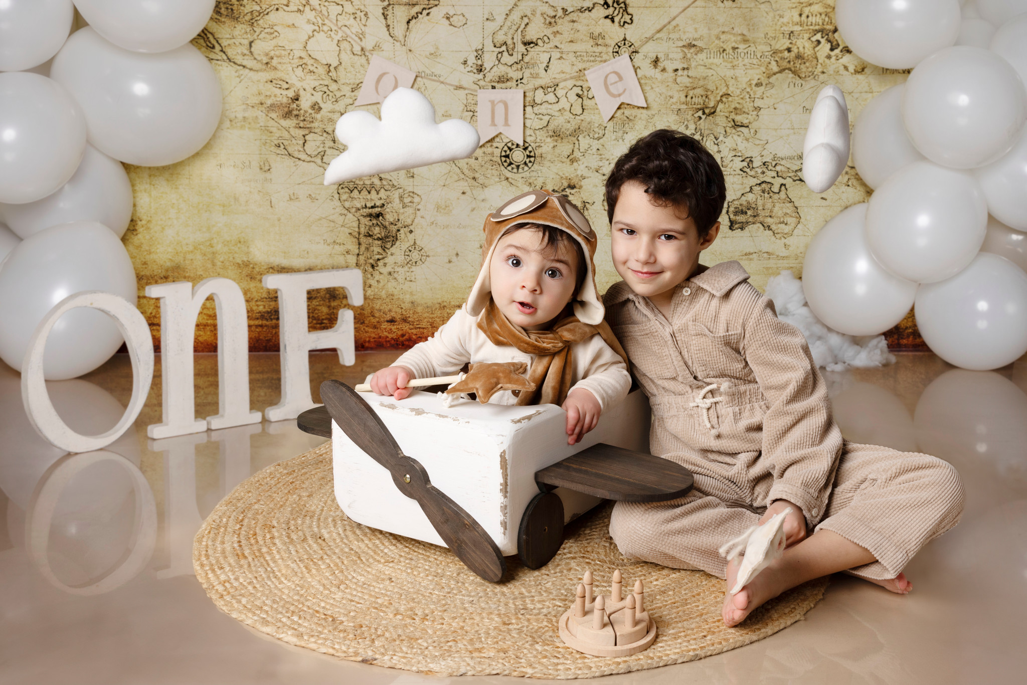 Bambino aviatore nell’aeroplanino di legno con il fratello maggiore, fondale mappa antica e ghirlanda di palloncini — Bologna.
