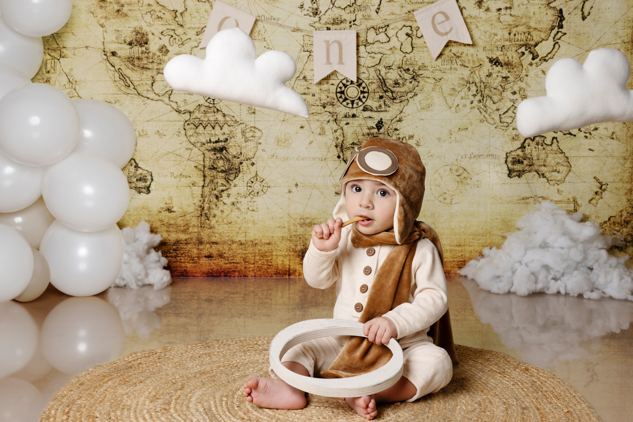 Bambino con cappellino da aviatore gioca con una lettera di legno — set smash cake a tema esplorazione, mappa e palloncini.