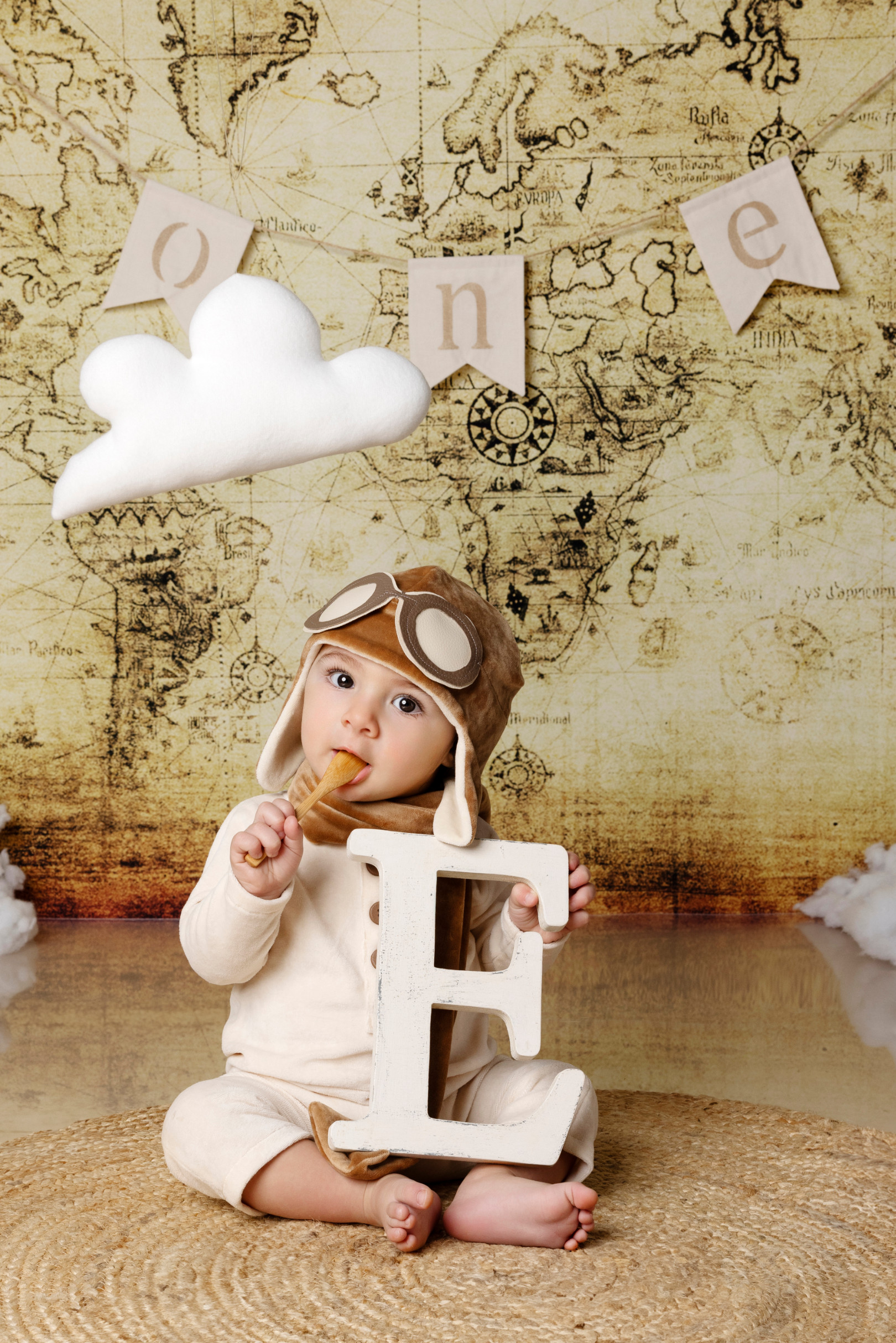 Bambino con cappello e occhiali da aviatore gioca con la lettera “E” di legno — set primo compleanno a tema viaggio, Bologna.