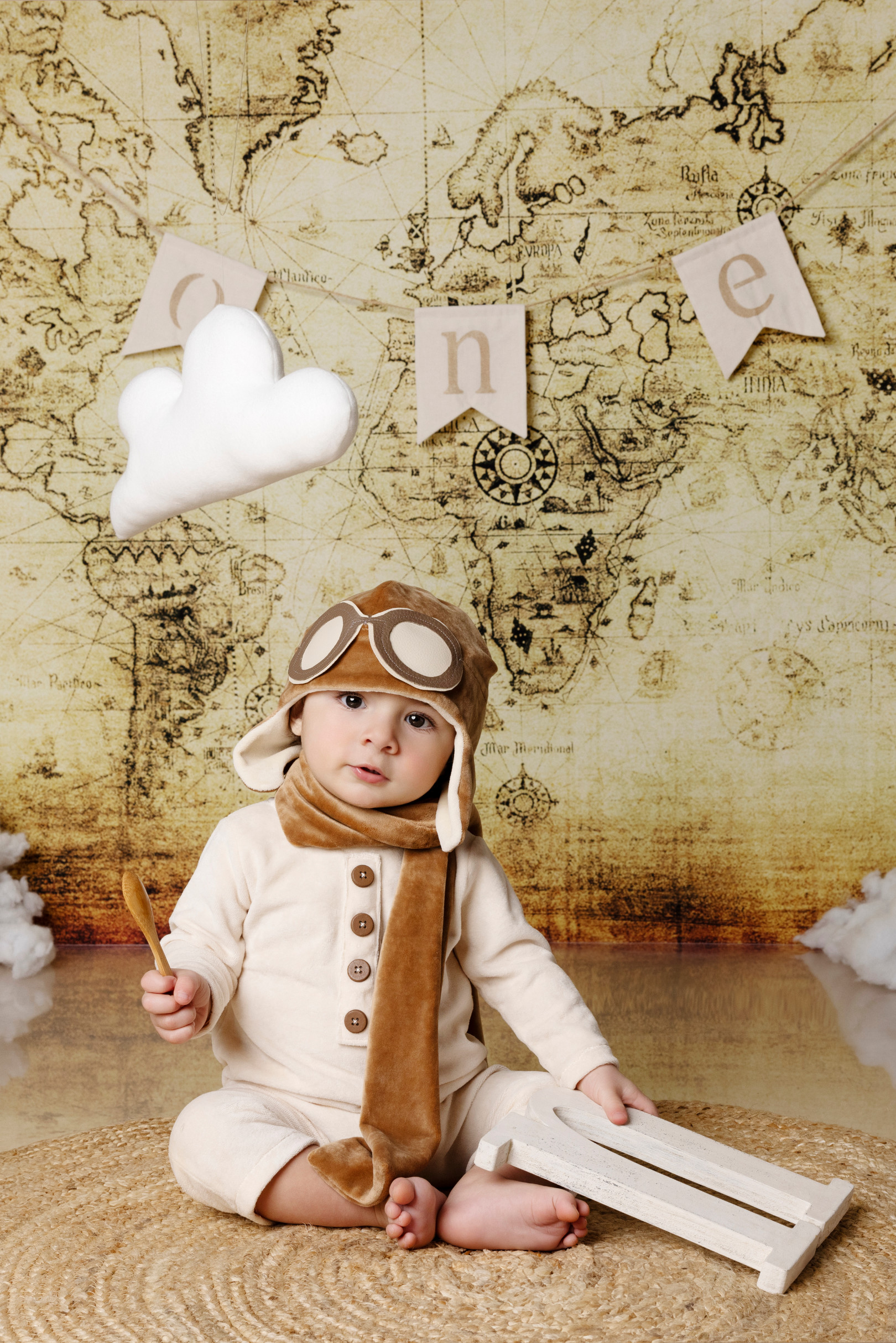 Bambino aviatore seduto tiene un giocattolo di legno — fondale mappa antica e nuvole, Bologna.